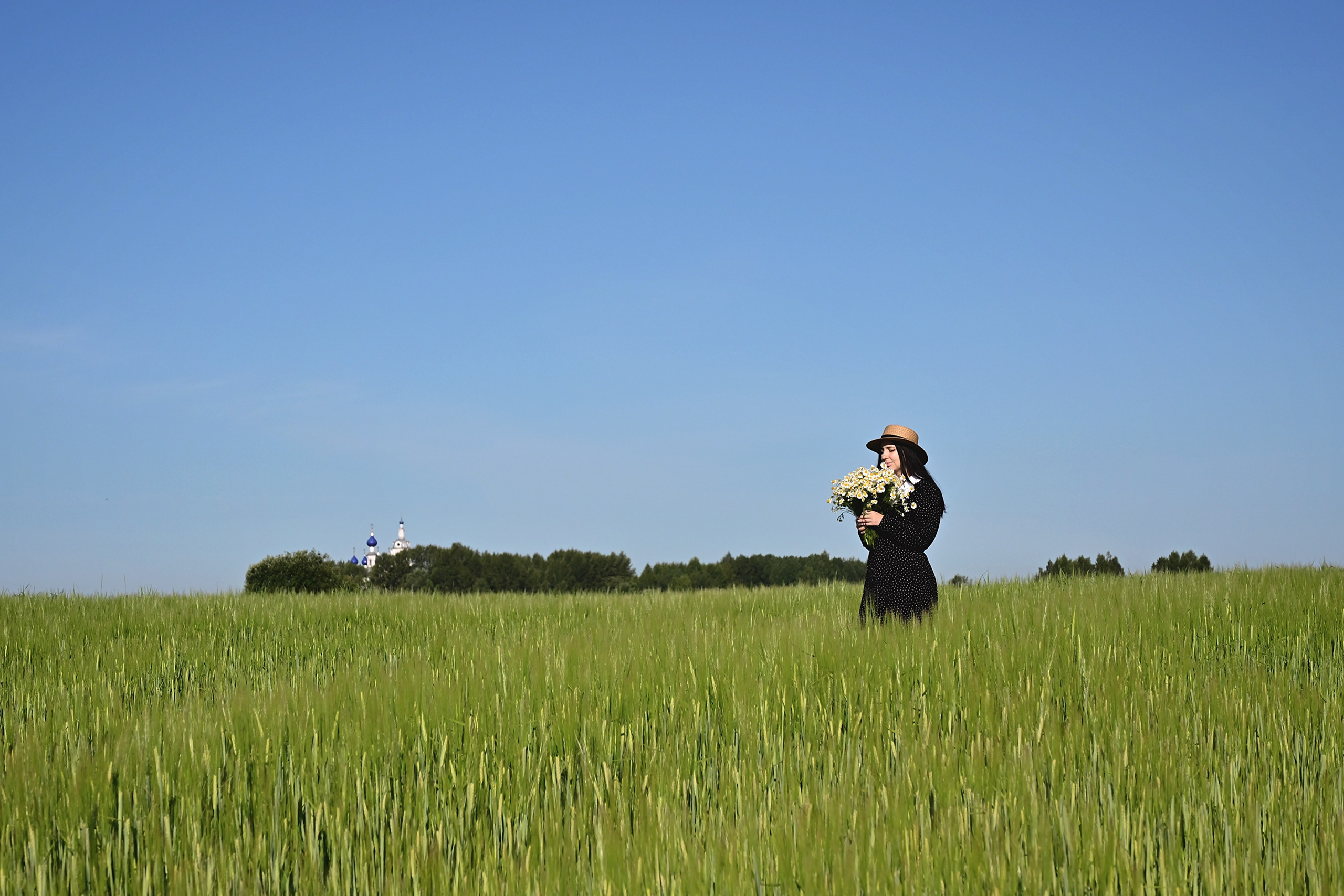 Девушка в шляпе в поле с букетом ромашек