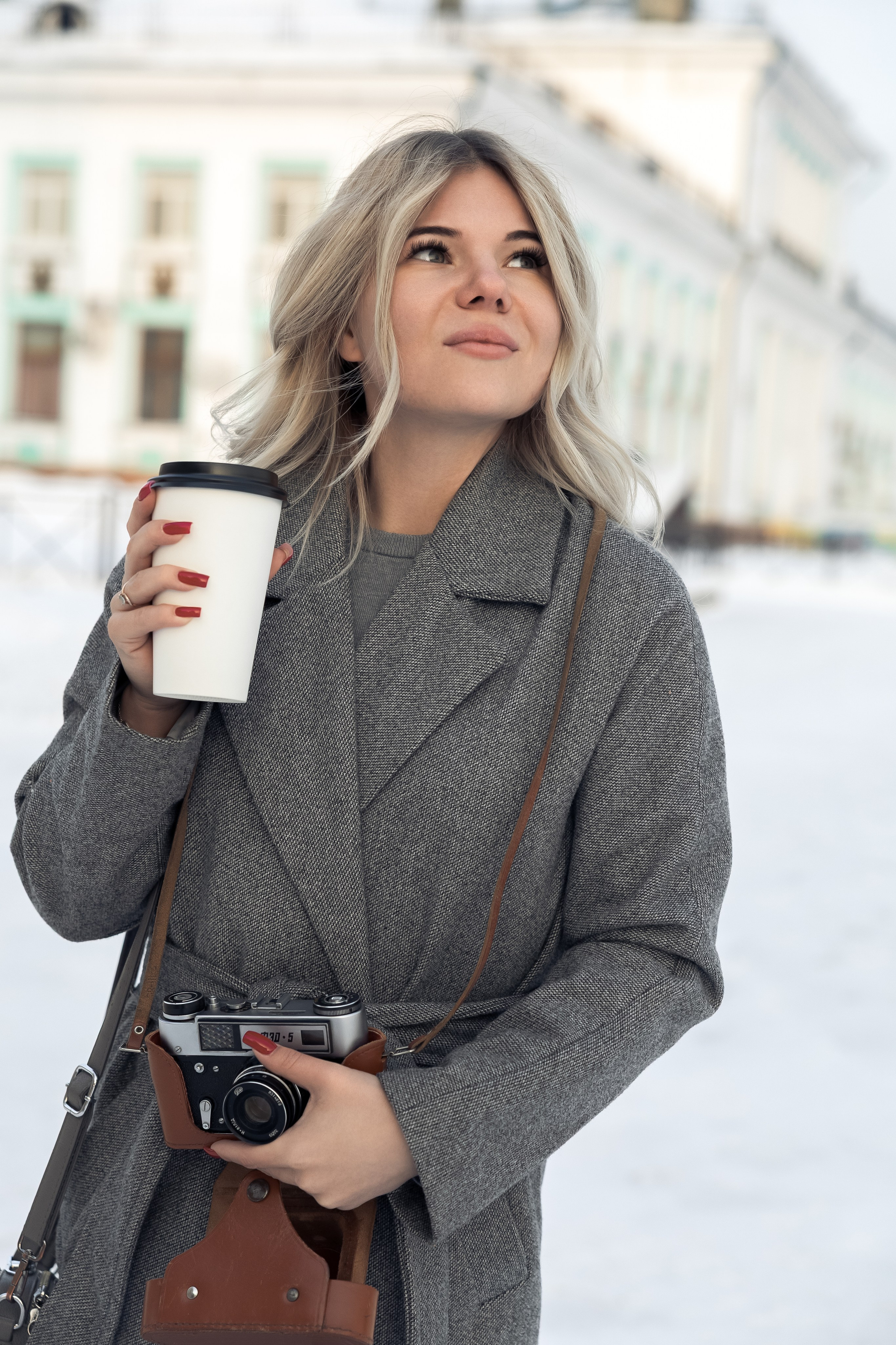 Девушка с чашкой кофе и фотокамерой на фоне городской архитектуры