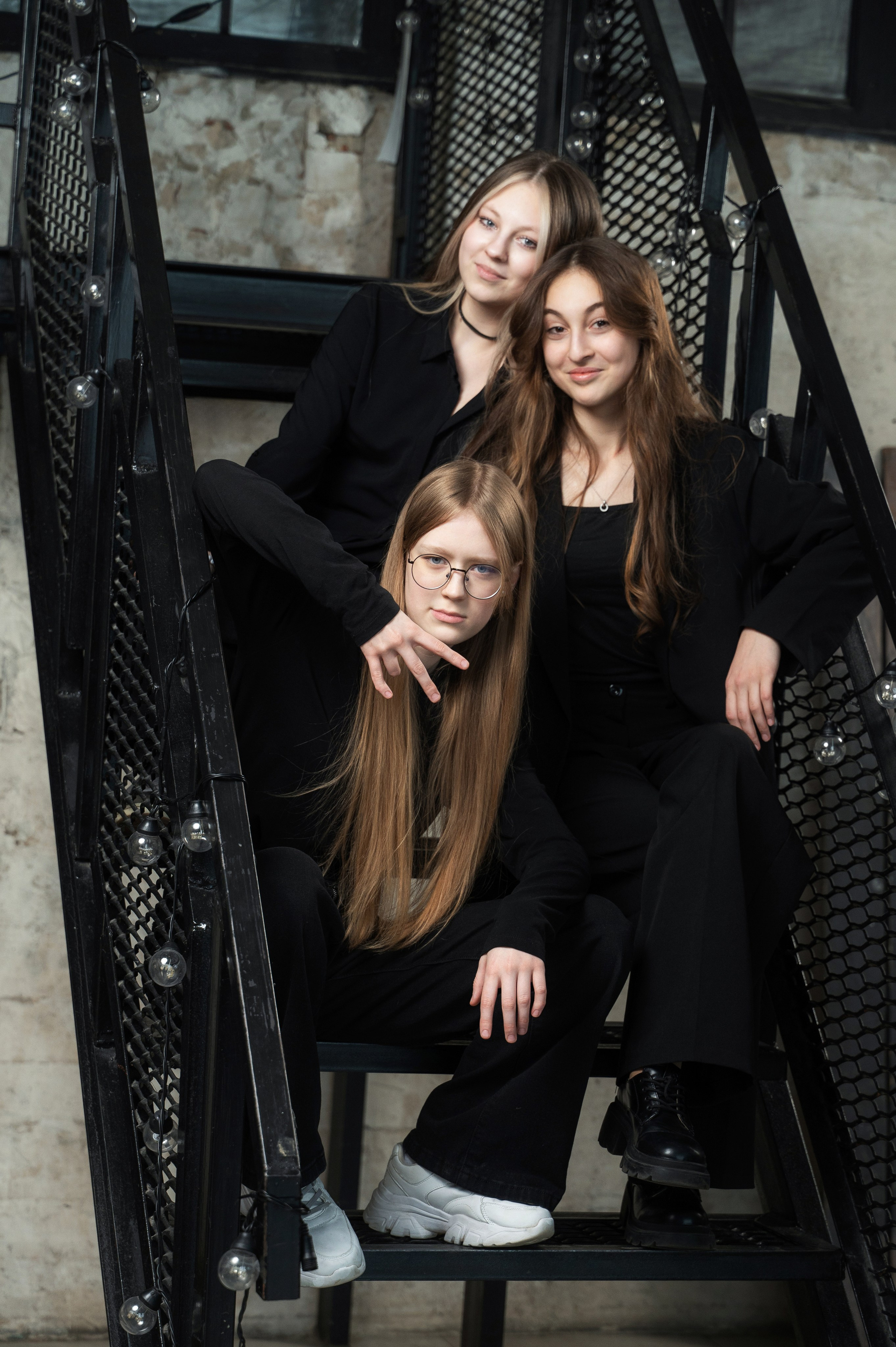 Три подруги расположились на черной металлической лестнице для стильного группового портрета.