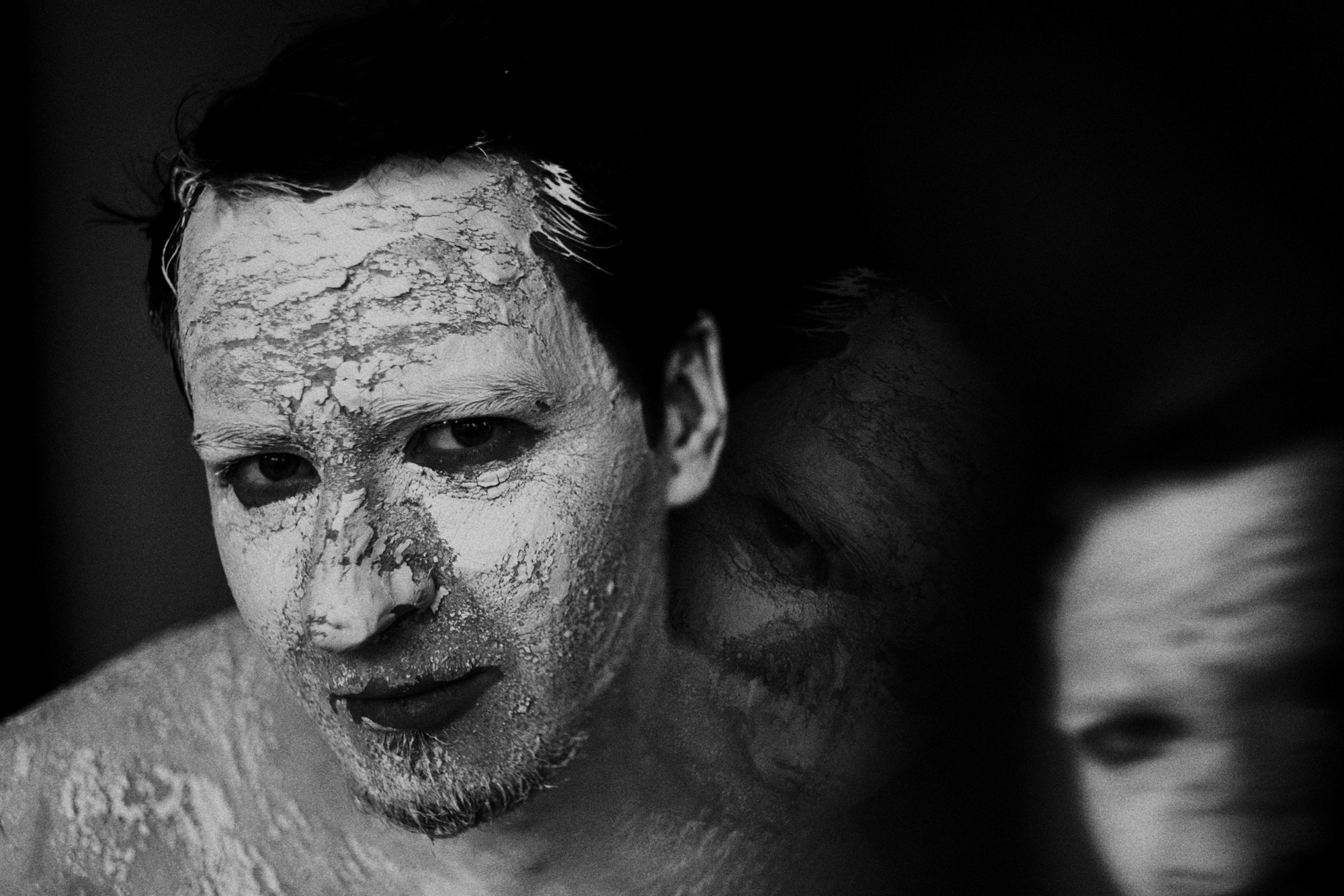 Крупный план мужского лица с художественным гримом, акцент на глазах и текстуре кожи, арт-фотография в черном ключе