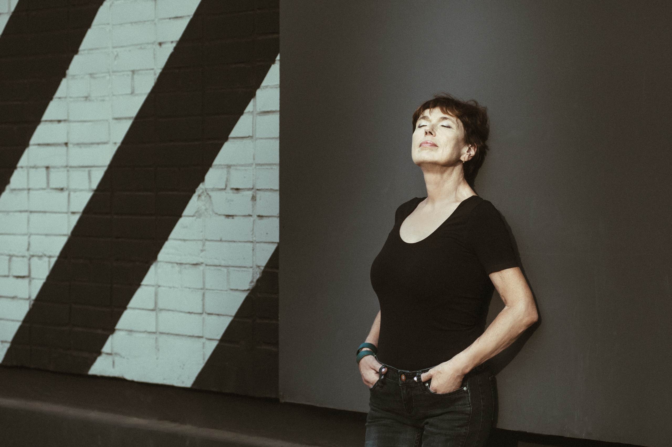 Летняя портретная фотосессия женщины в черной майке у стены