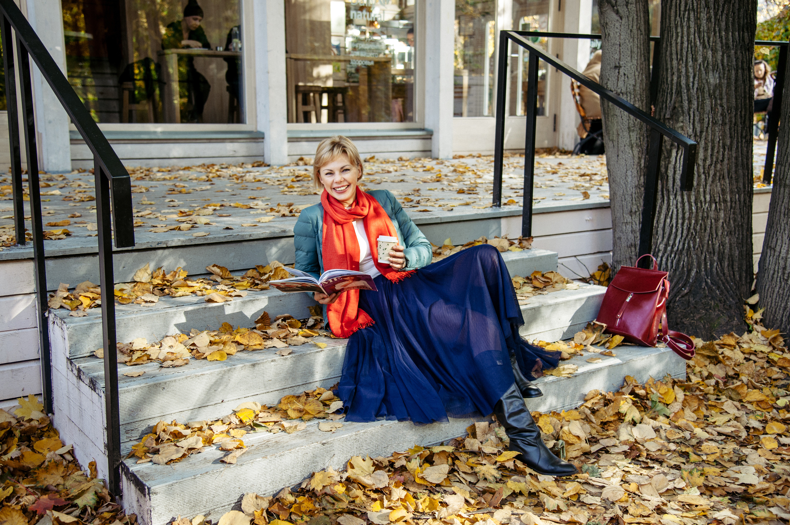 Осенняя портретная фотосессия женщины с красным шарфом на ступеньках у входа в кафе