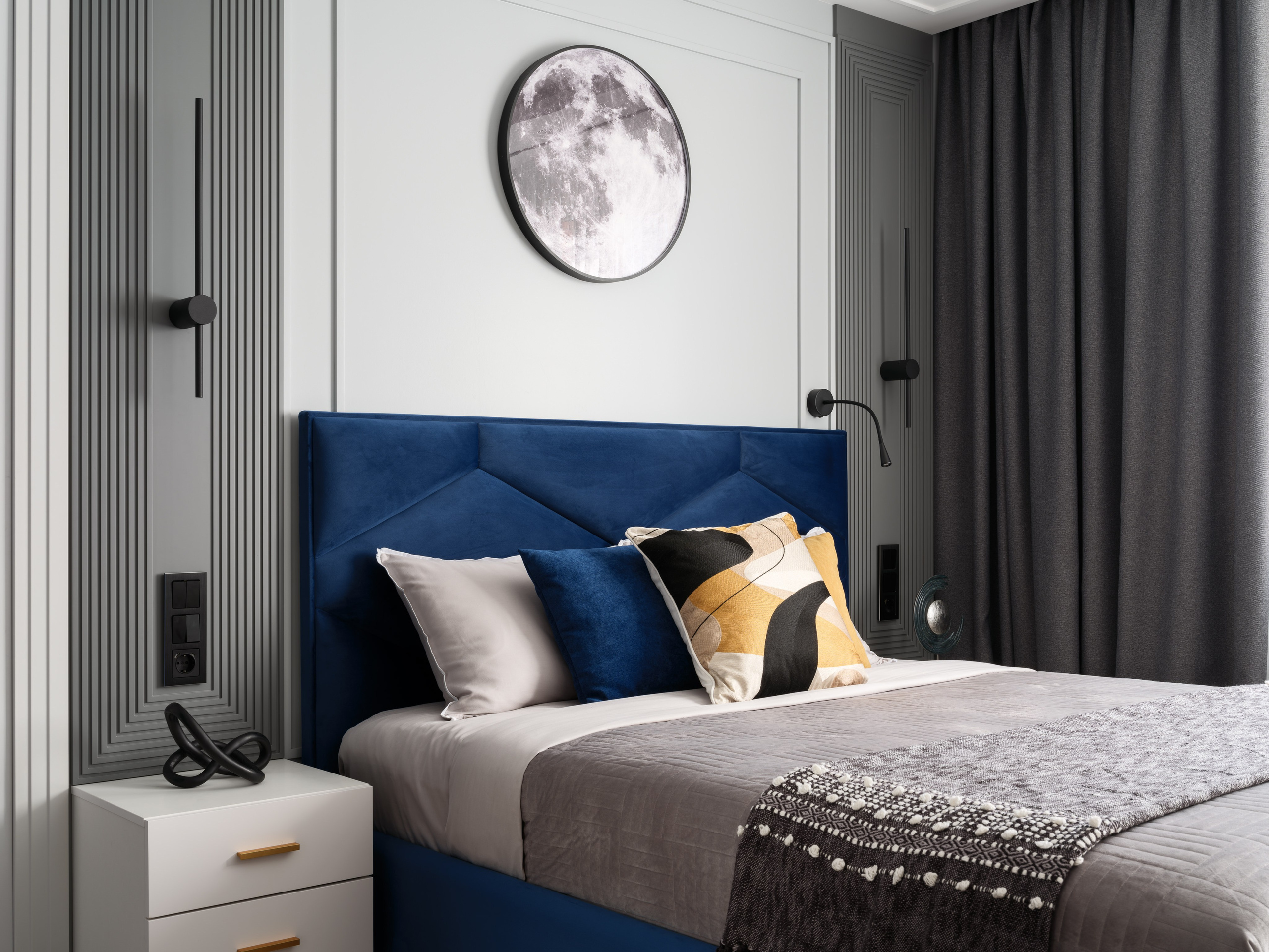 Современная спальня с серыми стенами, тёмными шторами, акцентным изголовьем кровати глубокого синего цвета и стильным текстилем. Автор проекта — дизайнер Евгения Ермошина, профессиональная фотосъёмка выполнена Сергеем Денисенко.