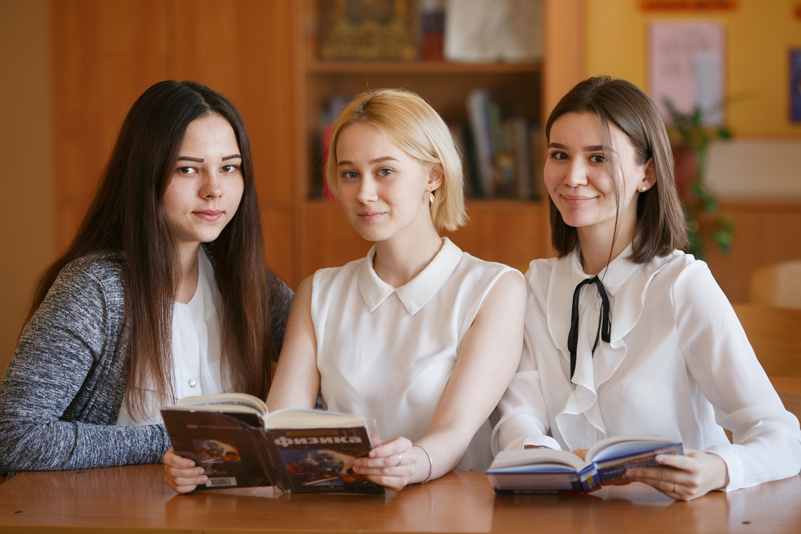 Три школьницы сидят за партой с книгой