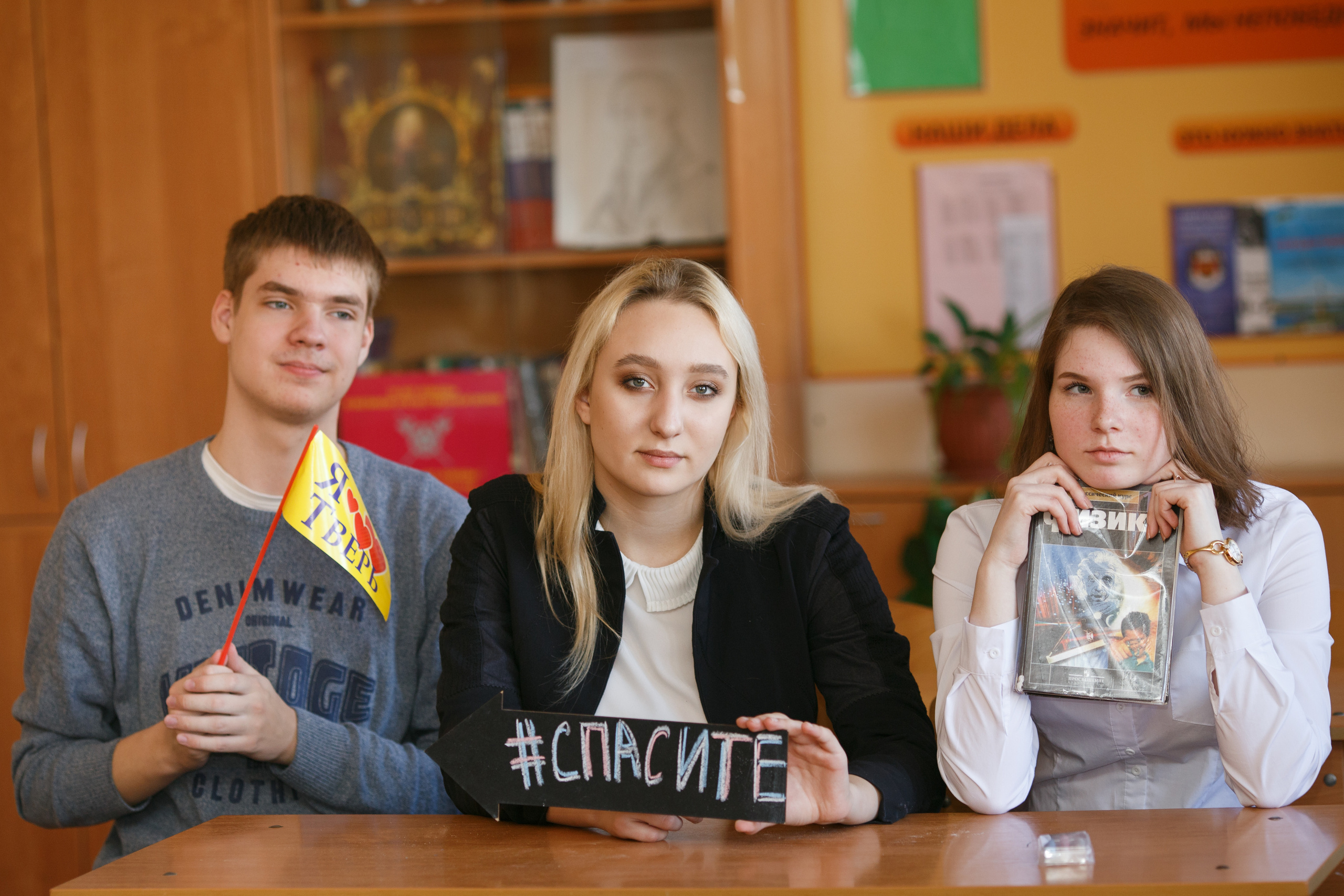 Школьники сидят за партой с табличкой "Спасите"