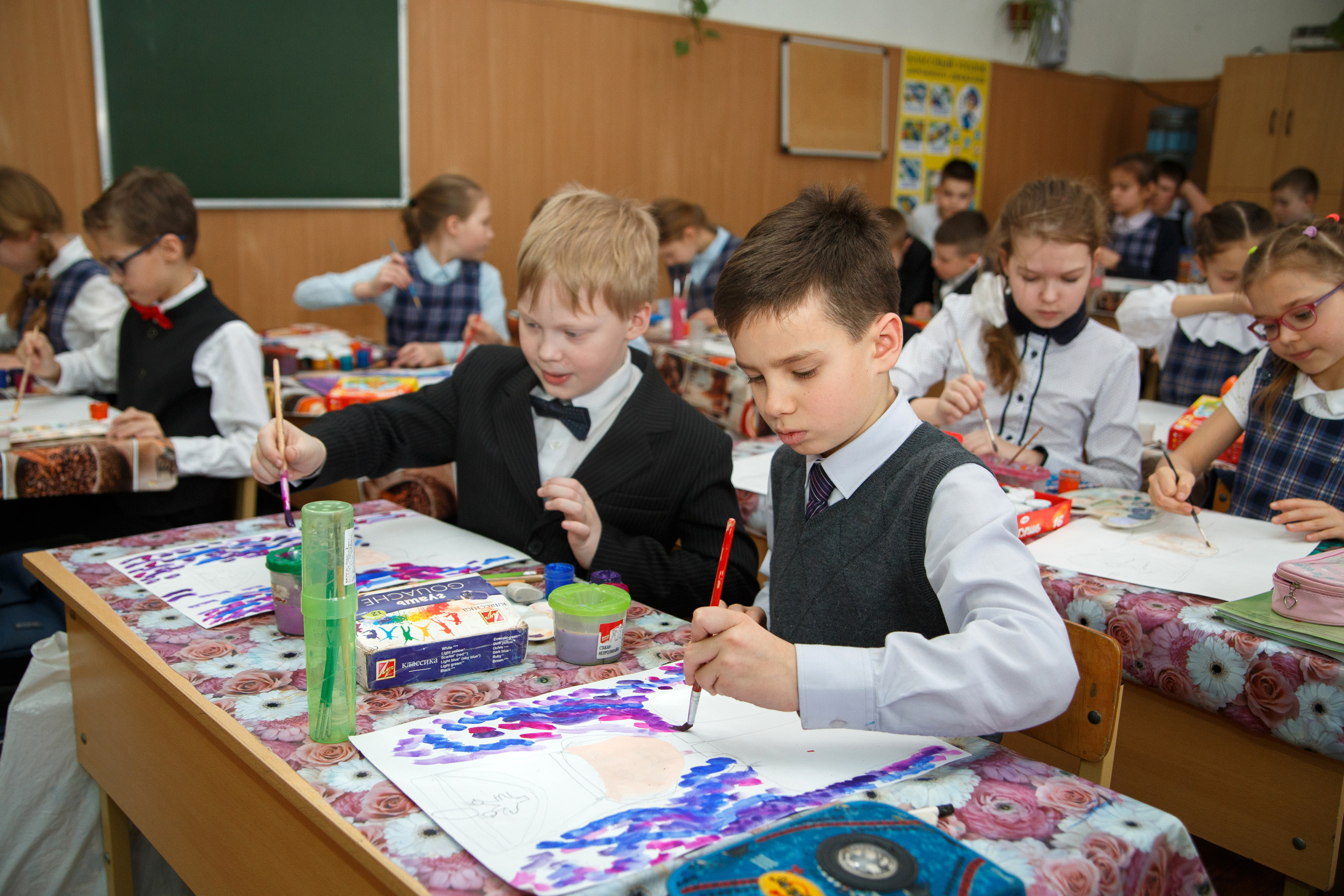 Четвероклассники на уроке изобразительного искусства сидят за партами и рисуют красками