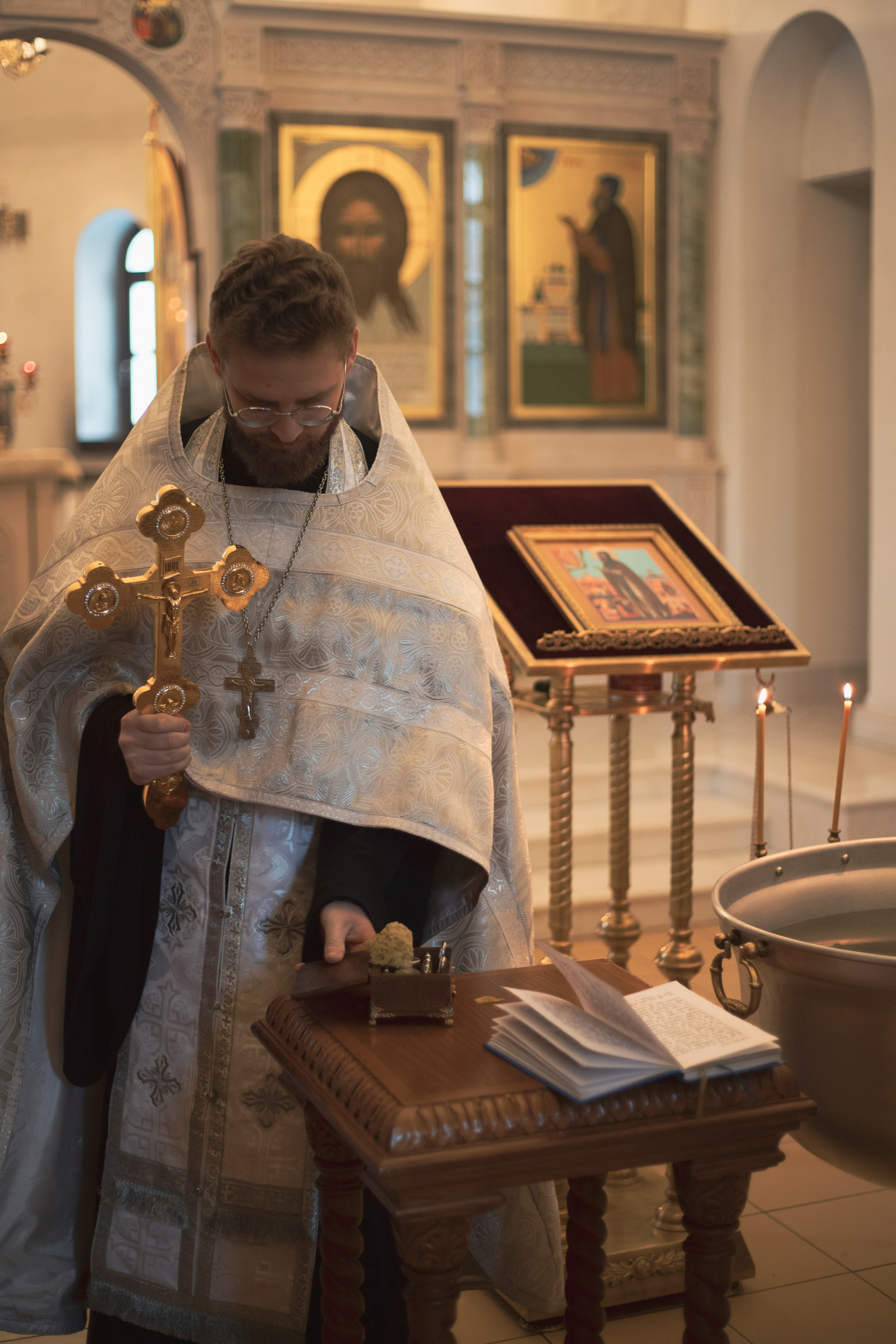 батюшка держит крест и готовится к крещению младенца