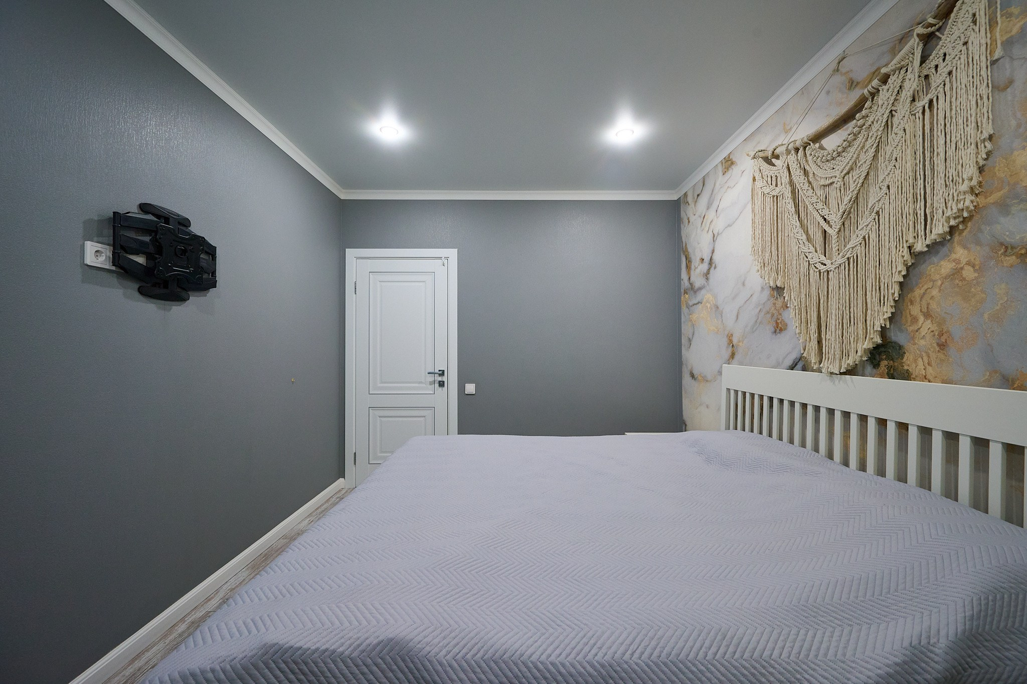 серые обои светлая кровать белая дверь и основание для телика