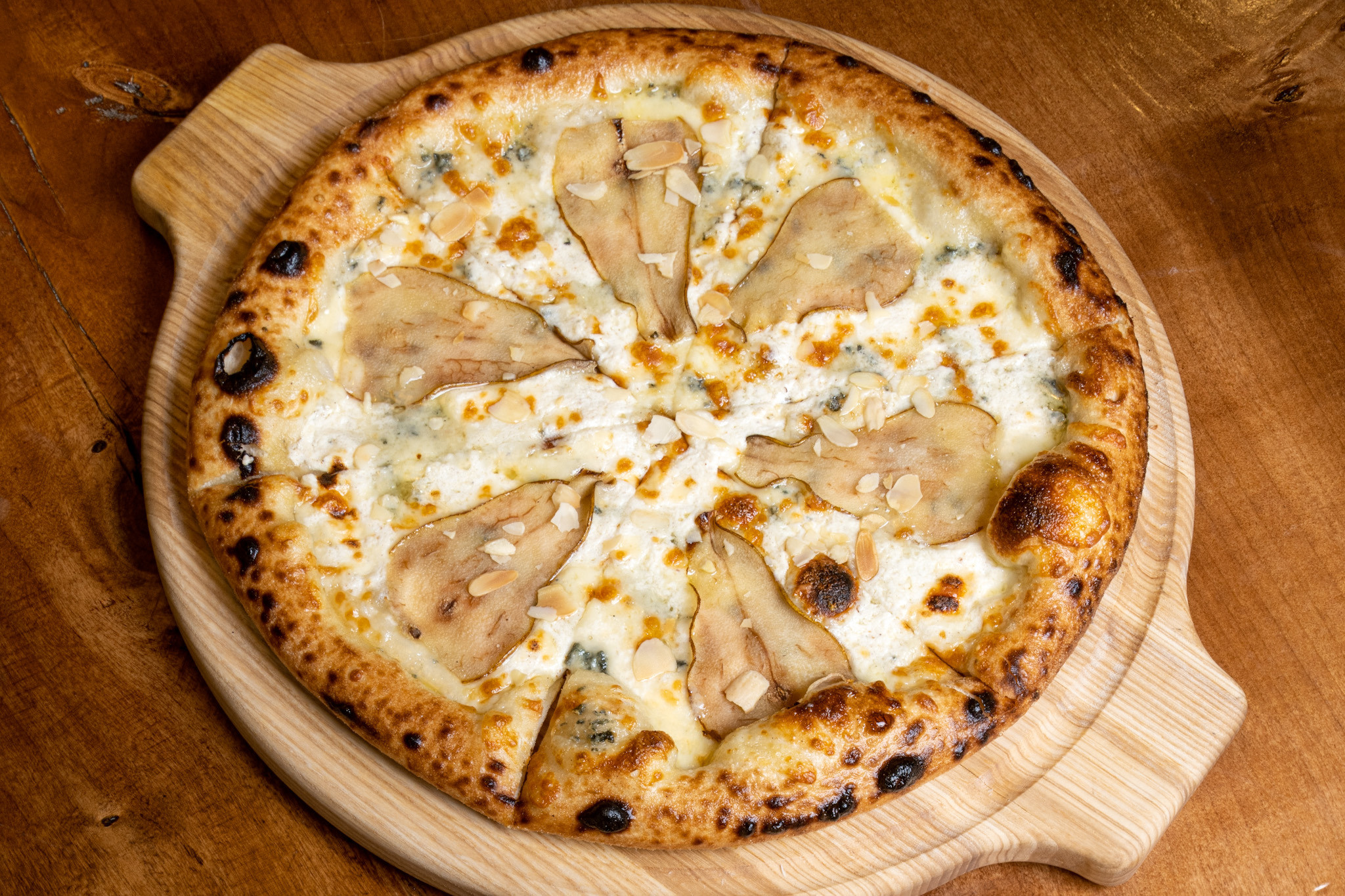 Круглая вкусная свежая пицца на деревянном подносе с кусочками запеченной груши