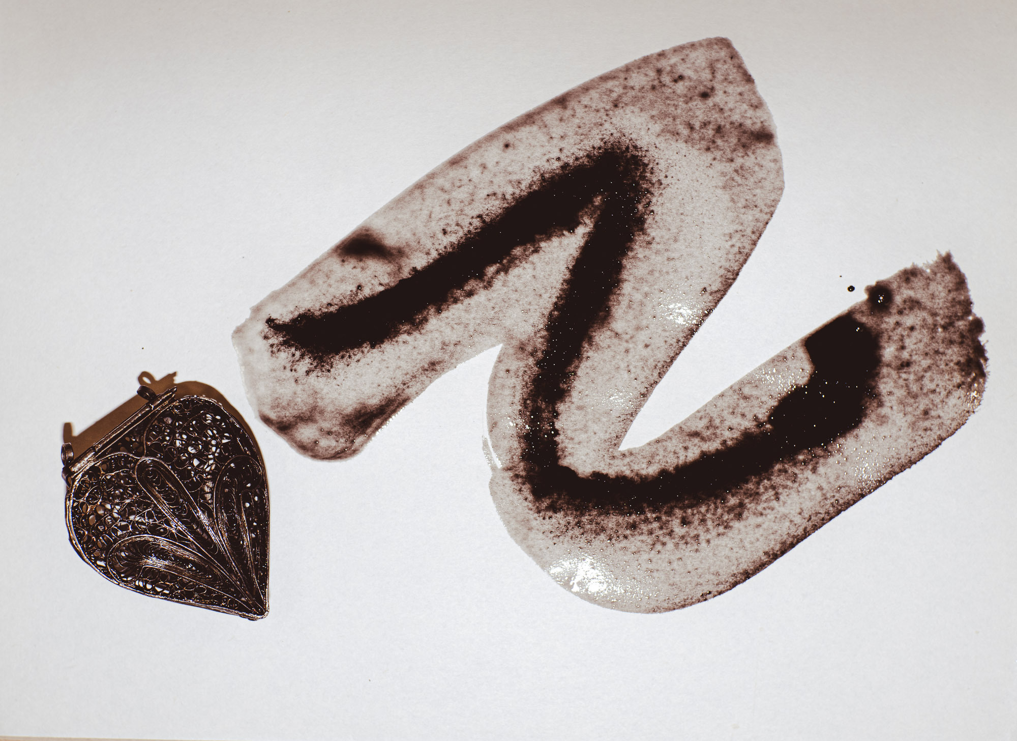 Вид сверху. Жирная линия от туши для каллиграфии, водный след, белый фон с яркой вспышкой. Кулон в форме сердца