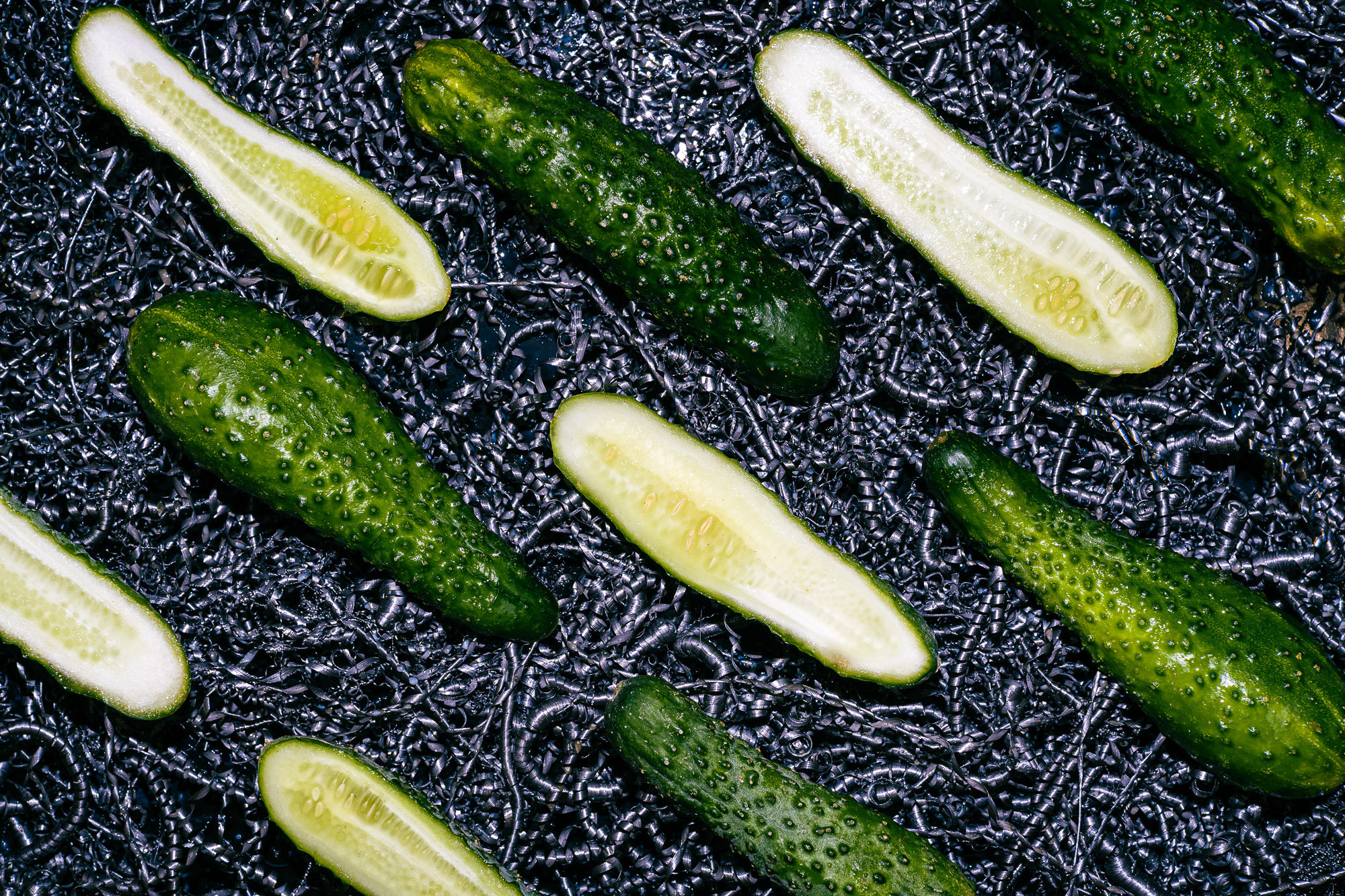 Вид сверху. Фон из металлической стружки. Огурцы зеленые разрезаны и выложены вдоль кадра. Художественная съемка