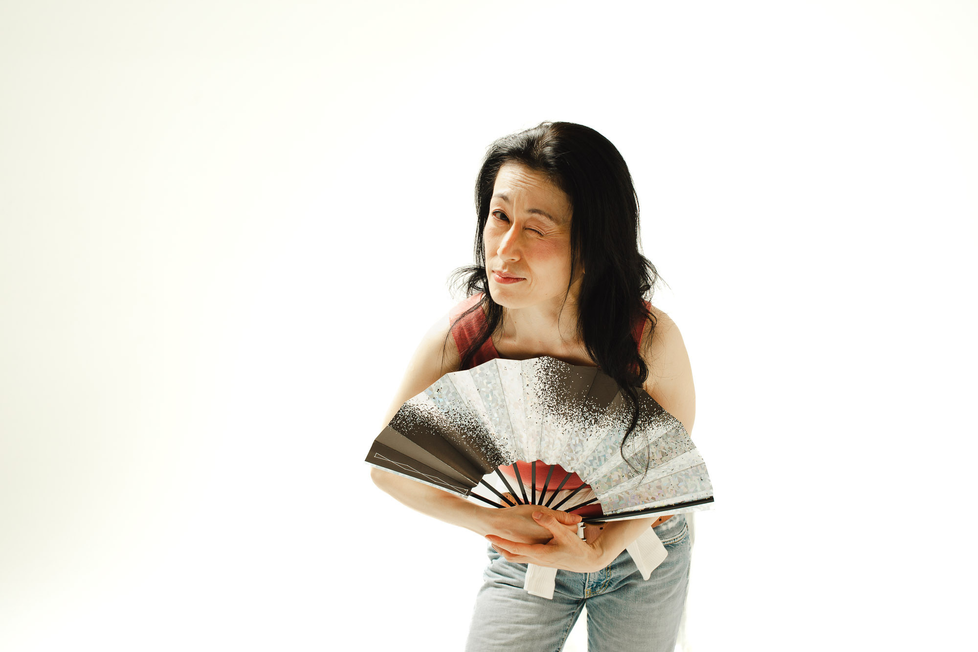 Японская актриса подмигивает зрителю в наклоне, белый фон, раскрытый веер, обычная одежда.