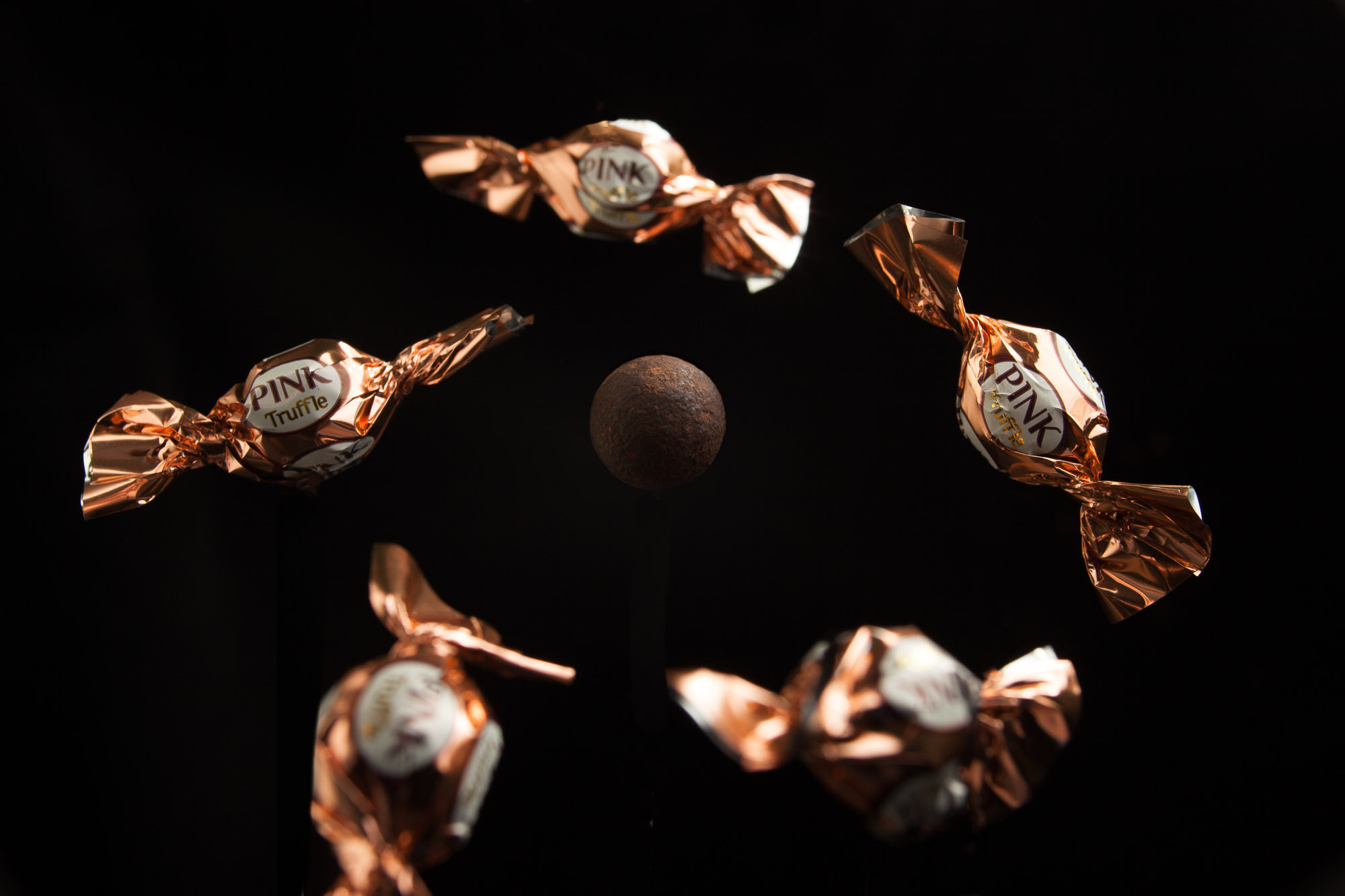 Золотые конфеты на черном фоне выстроились вокруг круглой коричневой конфеты словно она солнце