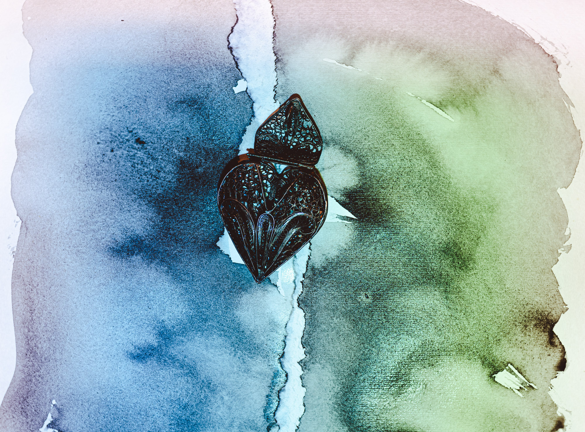 Вид сверху. Фон разделен на две половины, зеленый и голубые цвета. Водяные следы от чернил. Кулон в форме сердца в центре снимка