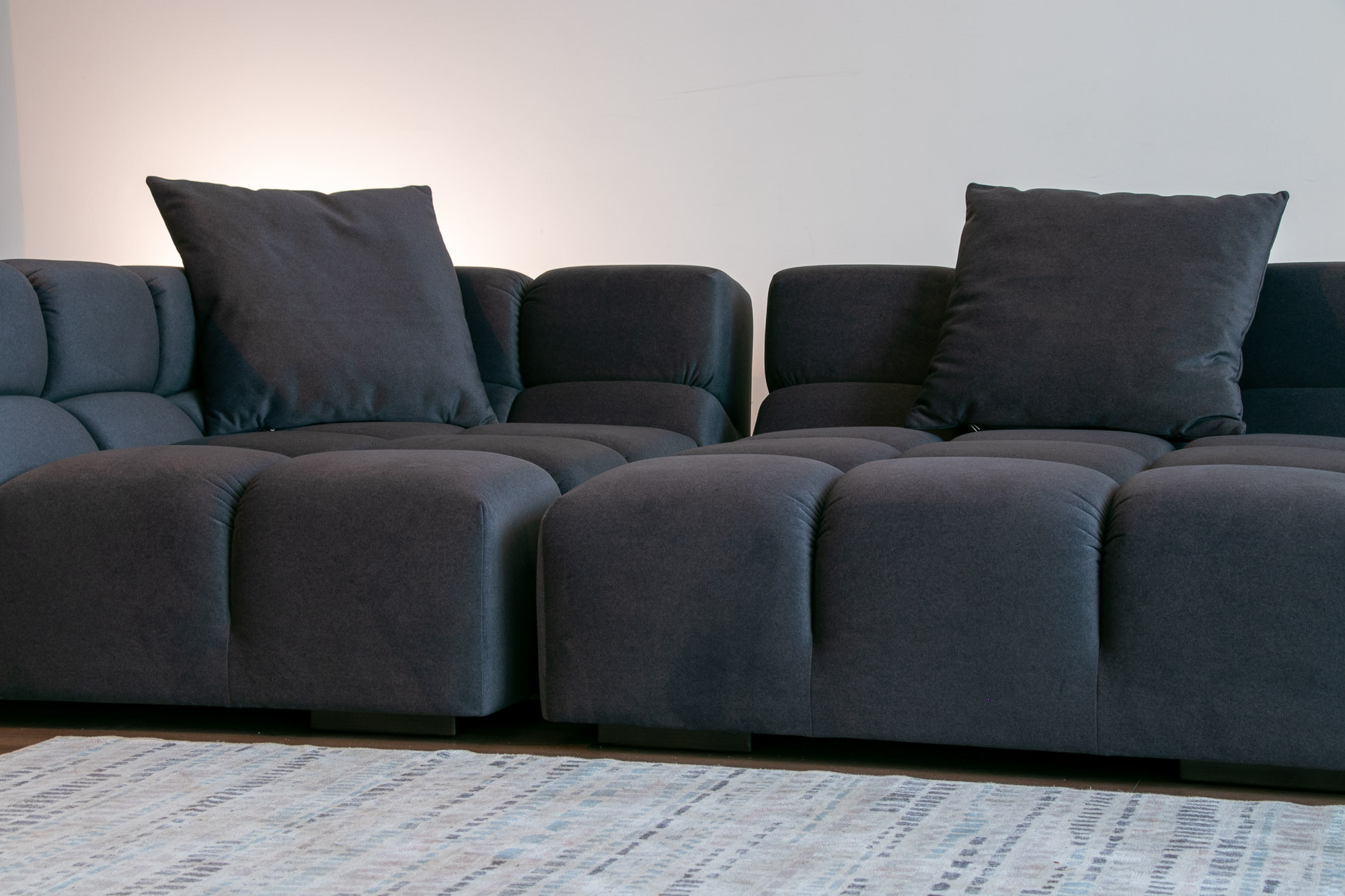 Черный диван, две секции сняты крупным планом, на заднем плане белый интерьер с вечерним освещением