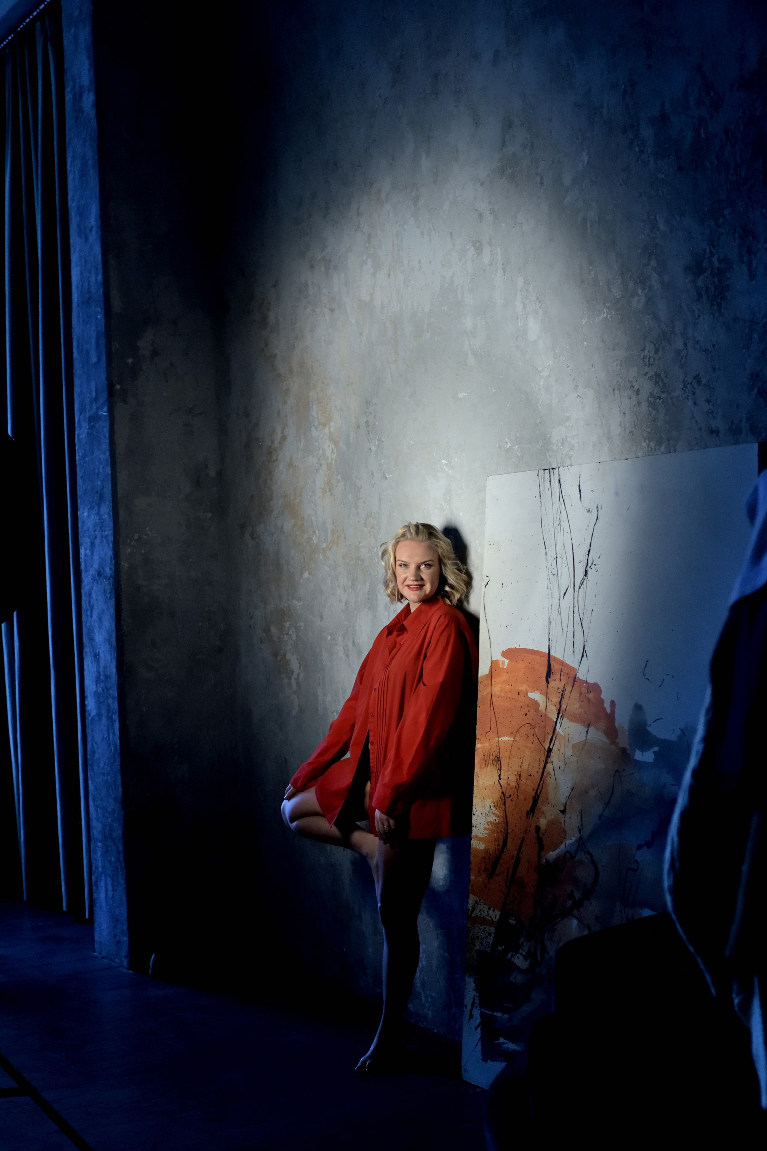 Девушка в красном позирует у серой стены.