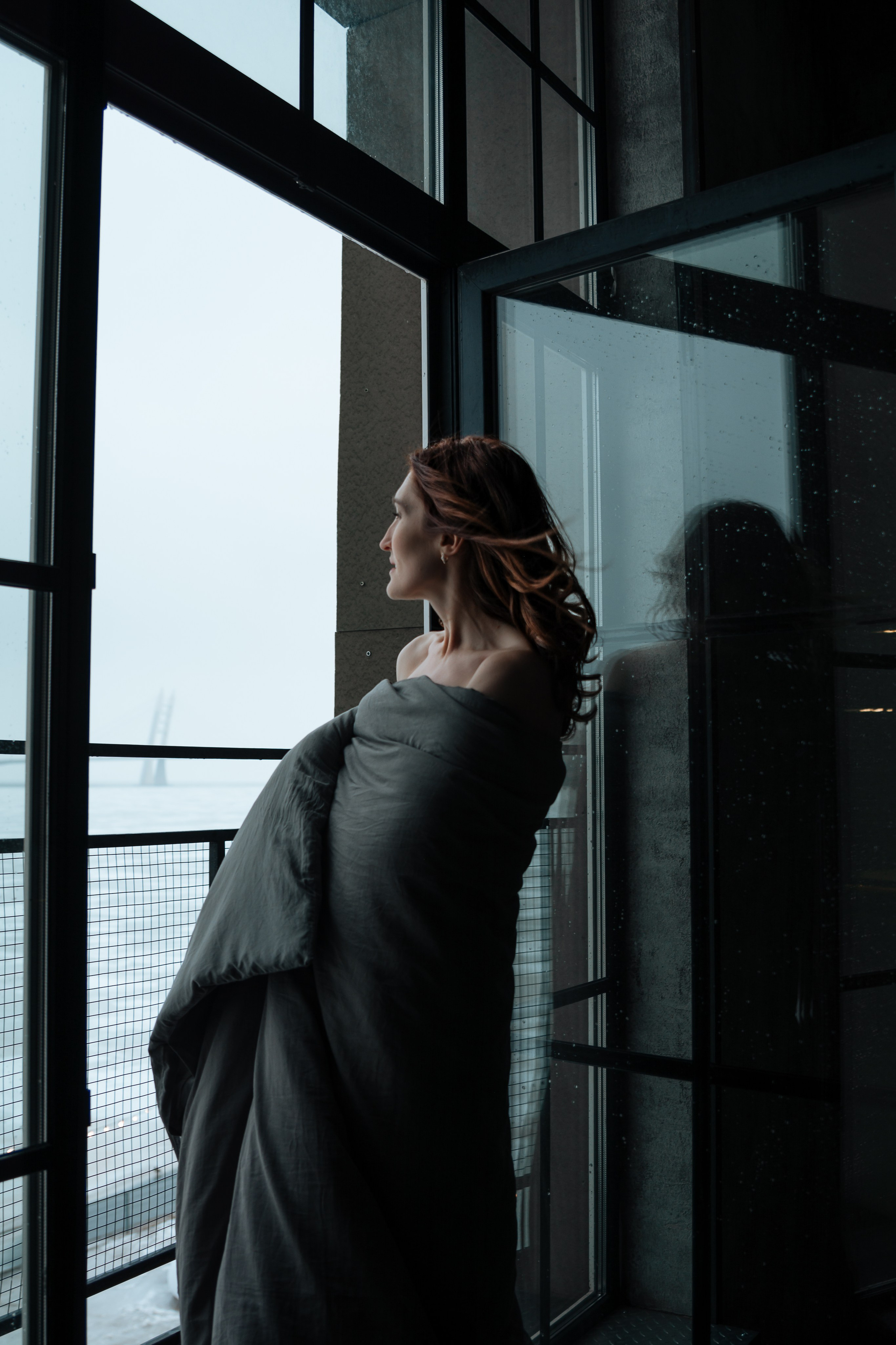 Легкий ветерок играет с прядями ее распущенных волос, овевая лицо. В полумраке комнаты ее кожа кажется нежной и бархатистой. Одеяло соскальзывает с плеча, обнажая изгиб шеи и ключицы.