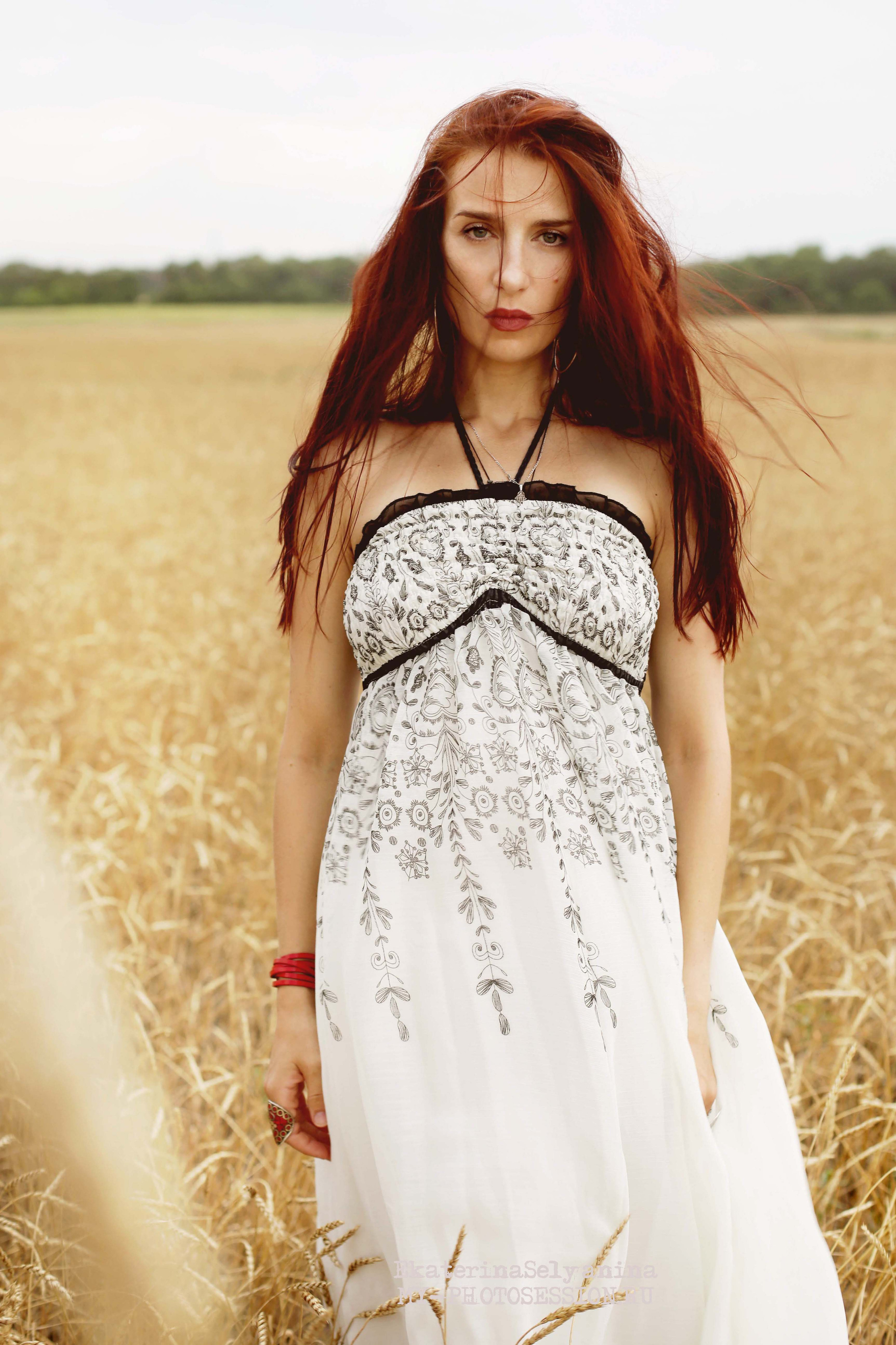 Рыжая длинноволосая женщина стоит в поле