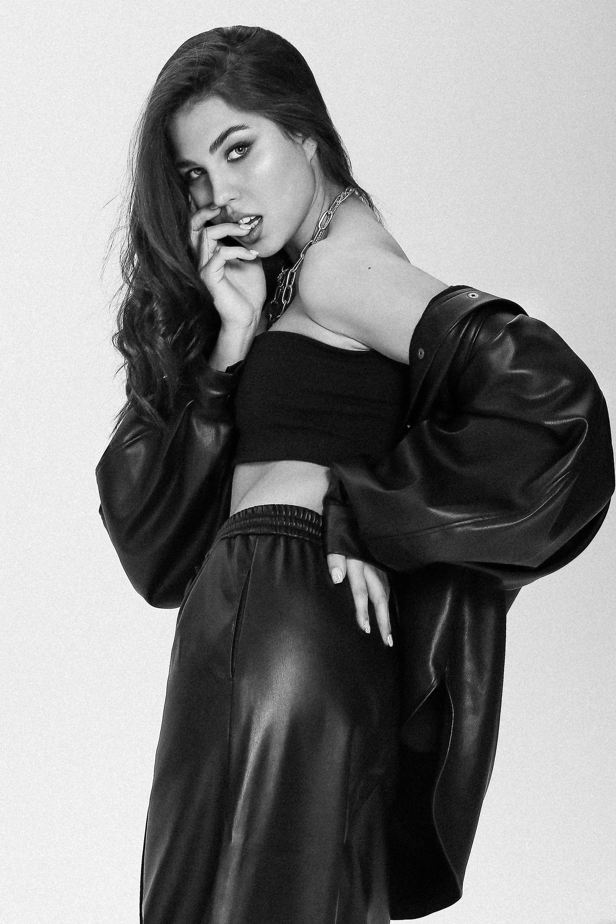 Девушка в кожаных брюках и куртке держит руки у лица