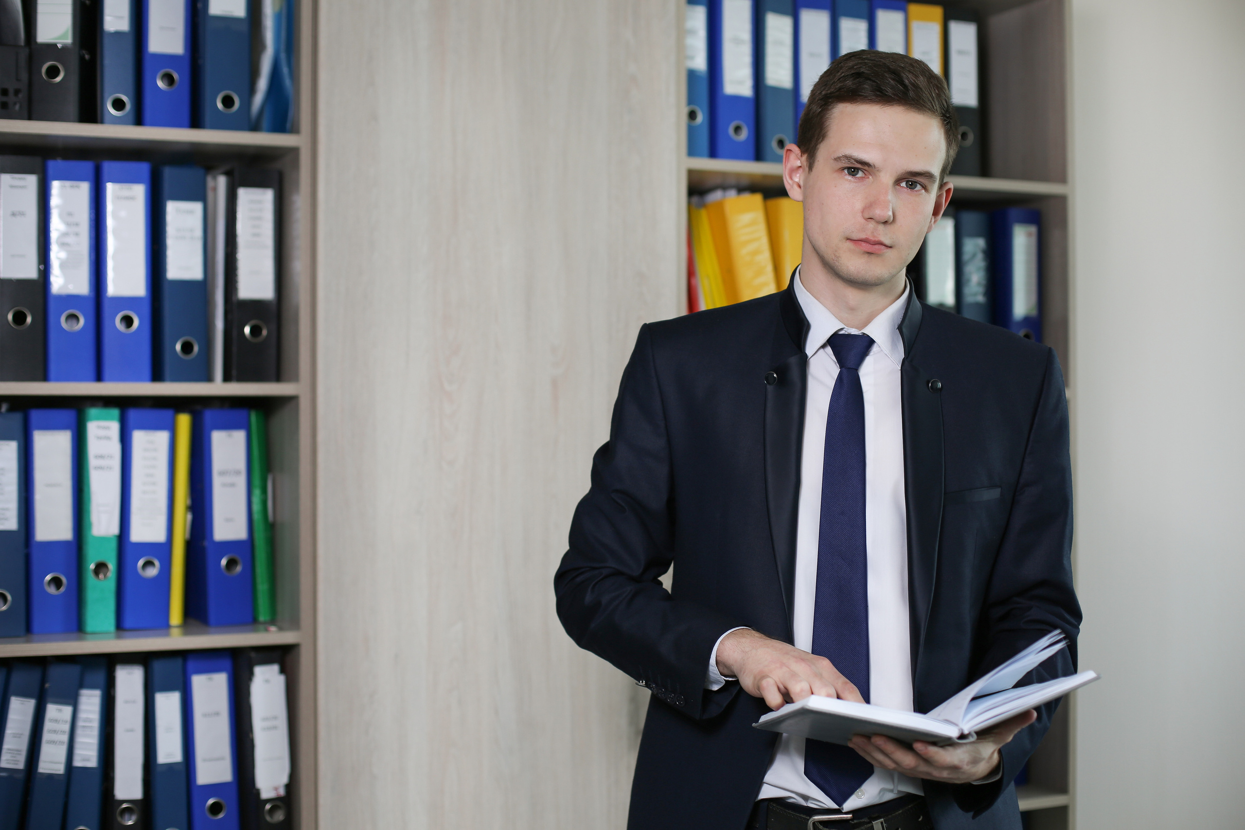 Молодой человек стоит около стеллажа с офисными документами