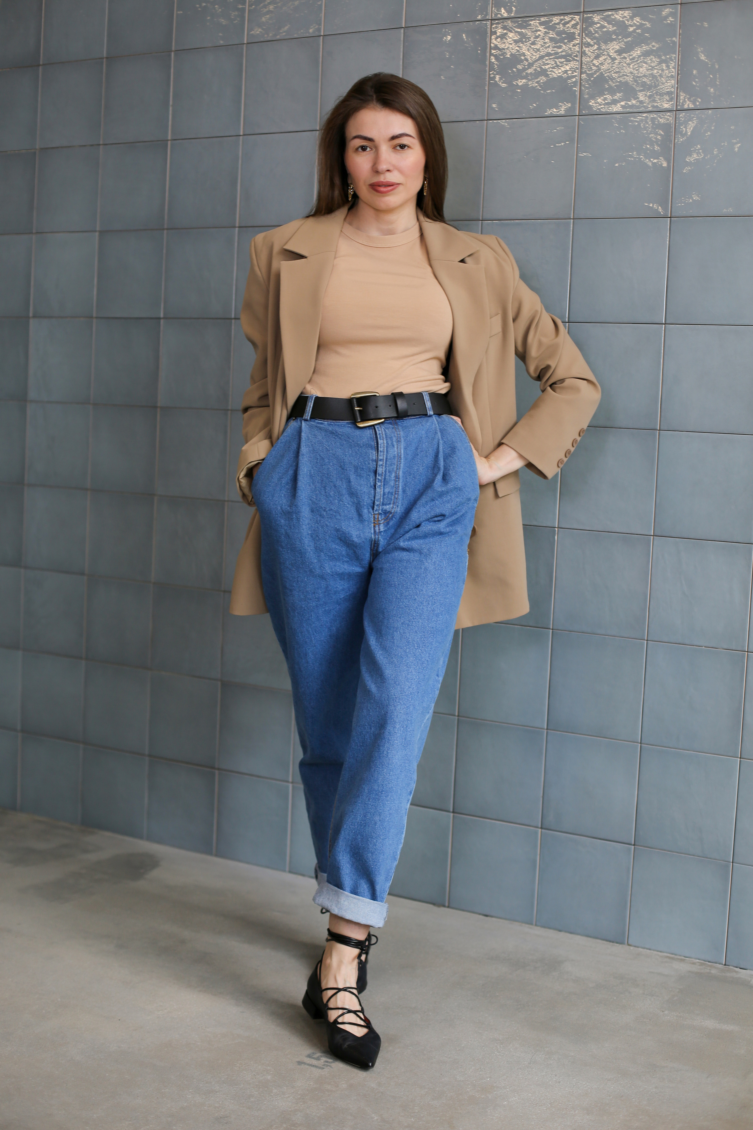 Красивая девушка в бежевом пиджаке стоит около стены из голубого кафеля