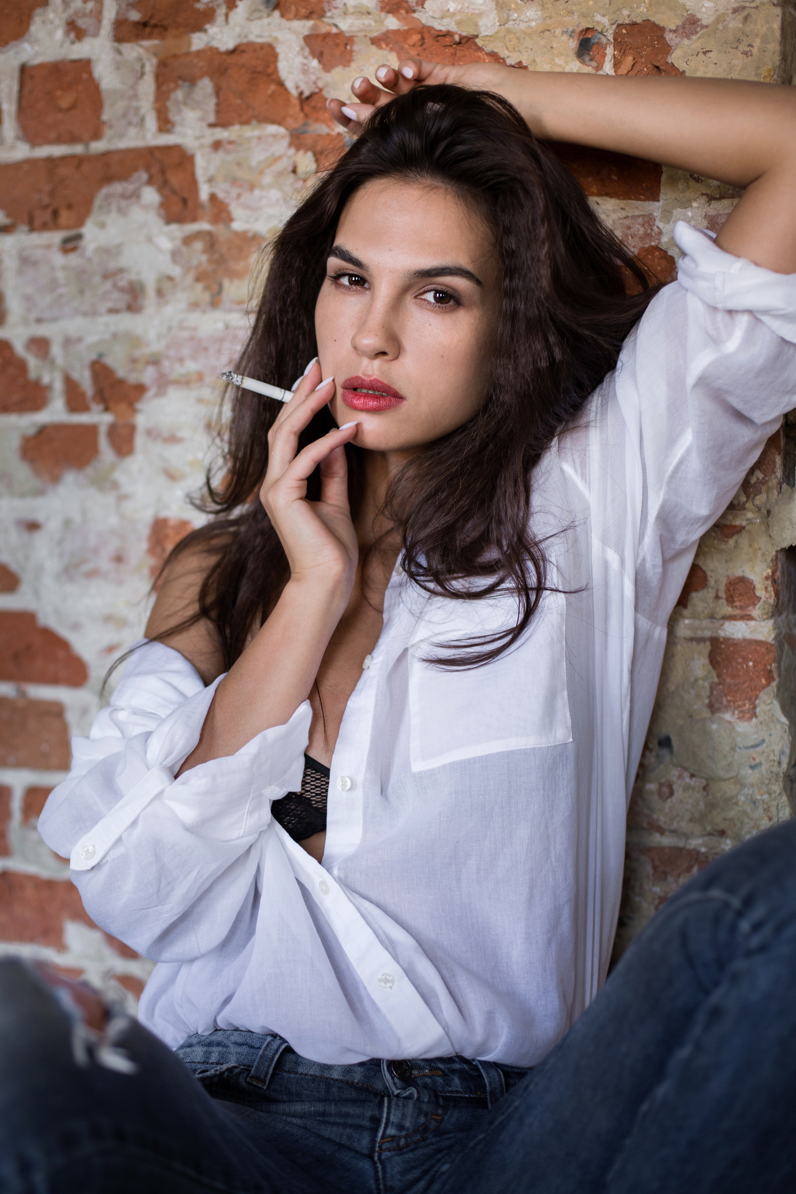 Красивая брюнетка в белой блузке  с красной помадой на губах позирует фотографу 