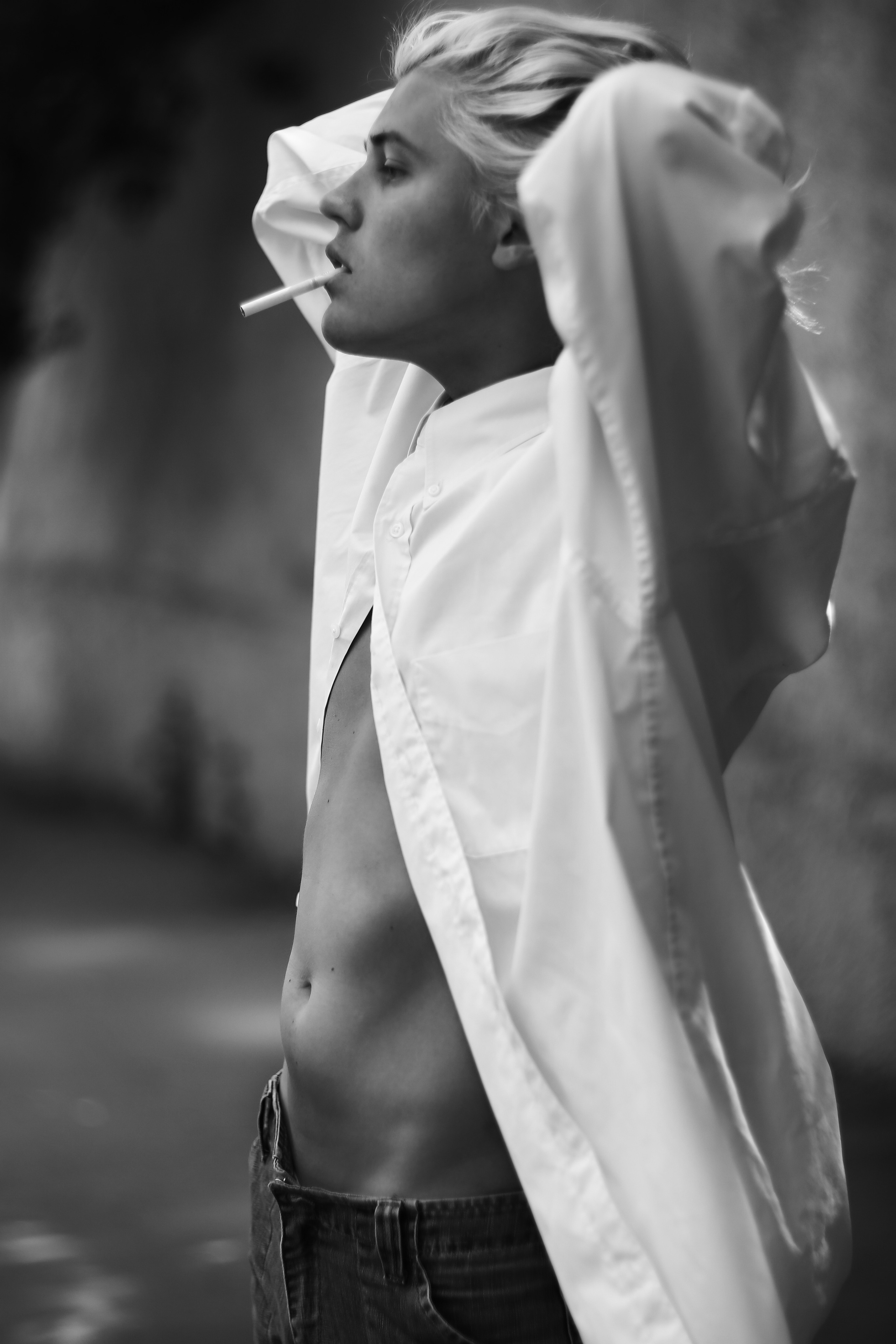 Парень в белой рубашке курит сигарету и мечтает