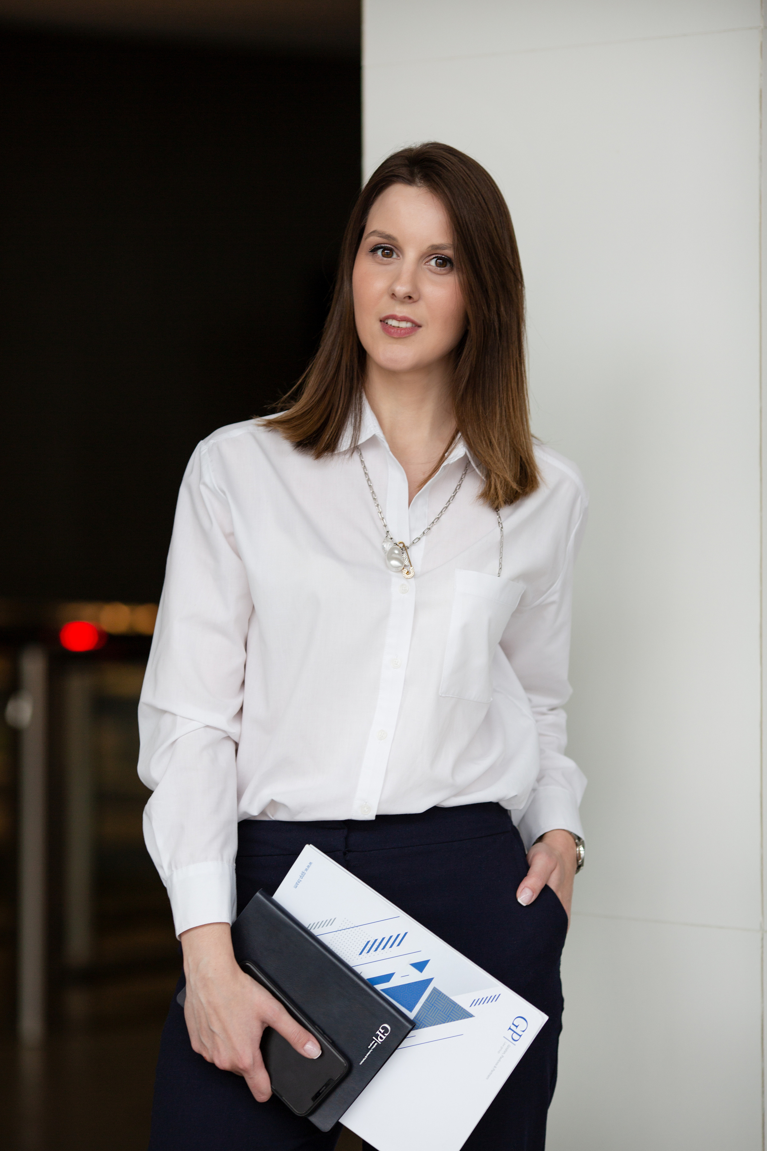 Девушка в белой блузке с папками в руках улыбается нам