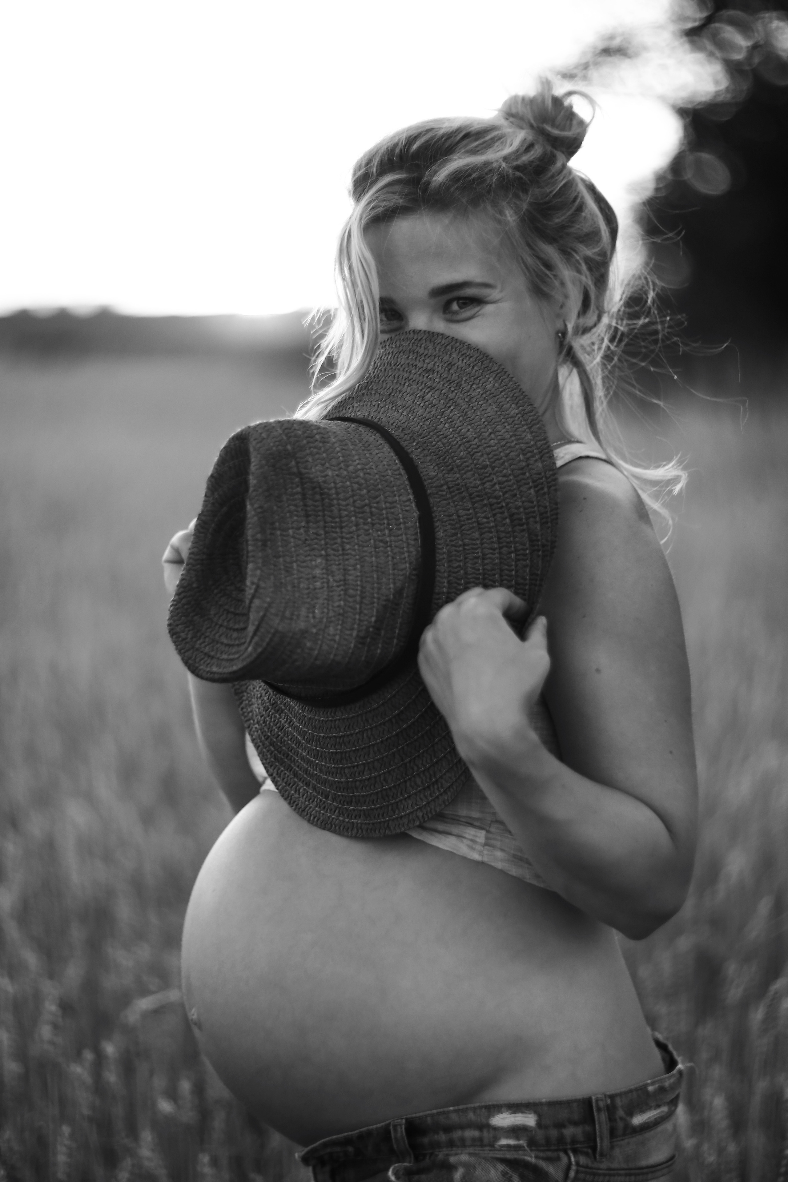 Беременяшка держит в руках соломенную шляпу она в поле