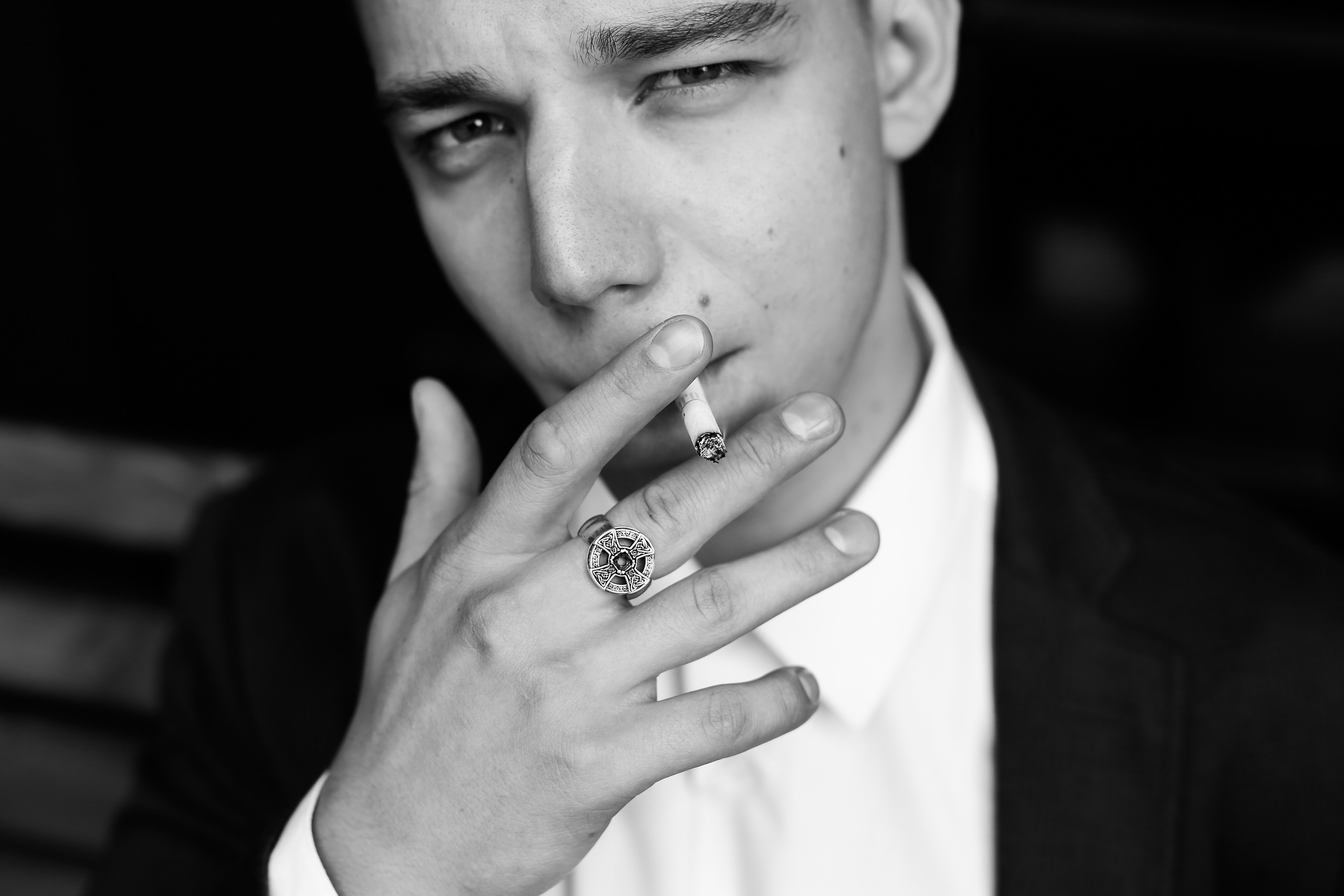 Парень курит сигарету на нем черный пиджак и белая мужская сорочка