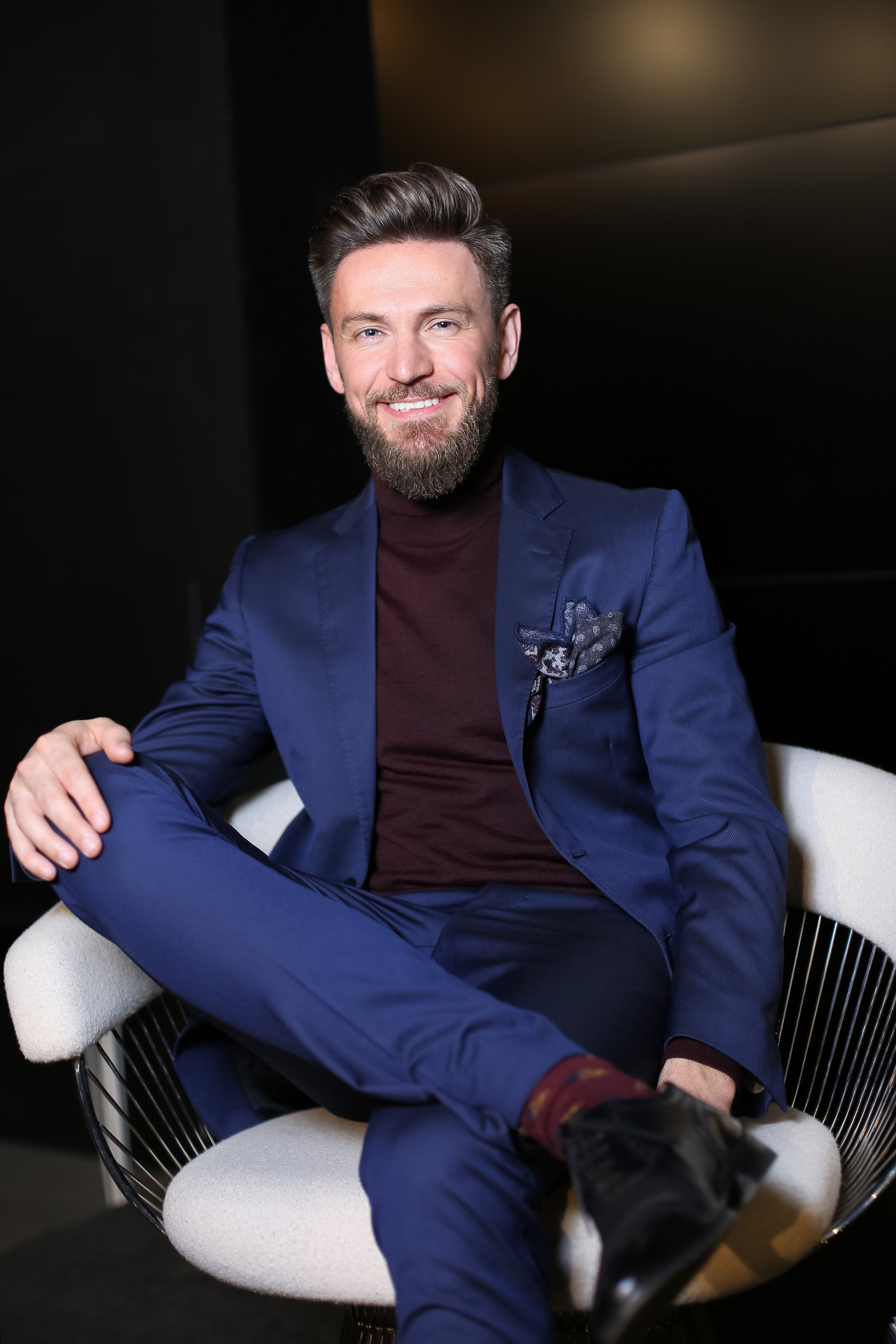 Мужчина ведущий в стильном костюме сидит в кресле