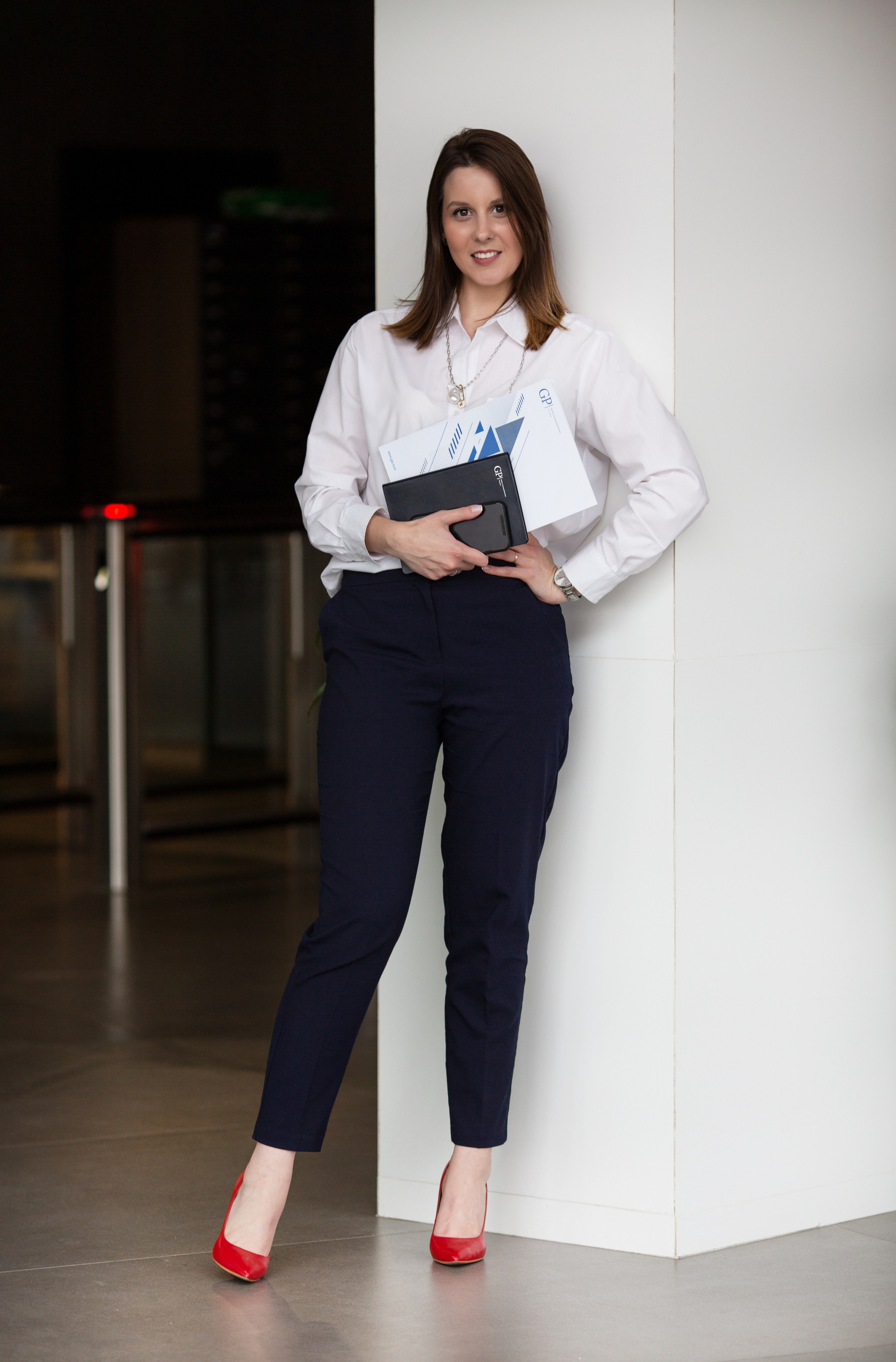 Красивая брюнетка в красных туфлях у белой стены