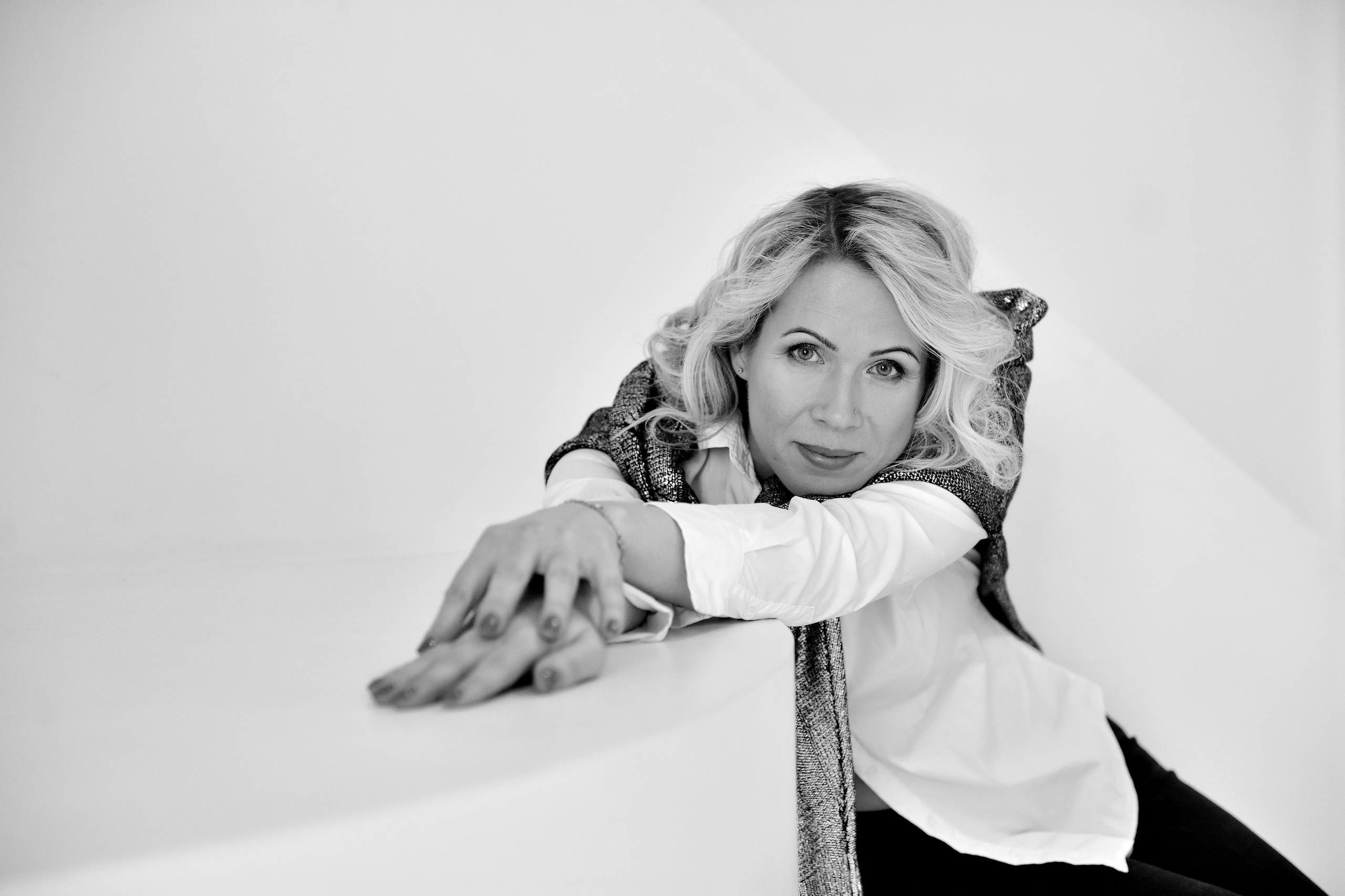 Блондинка в белой рубашке позирует в белой фотостудии.