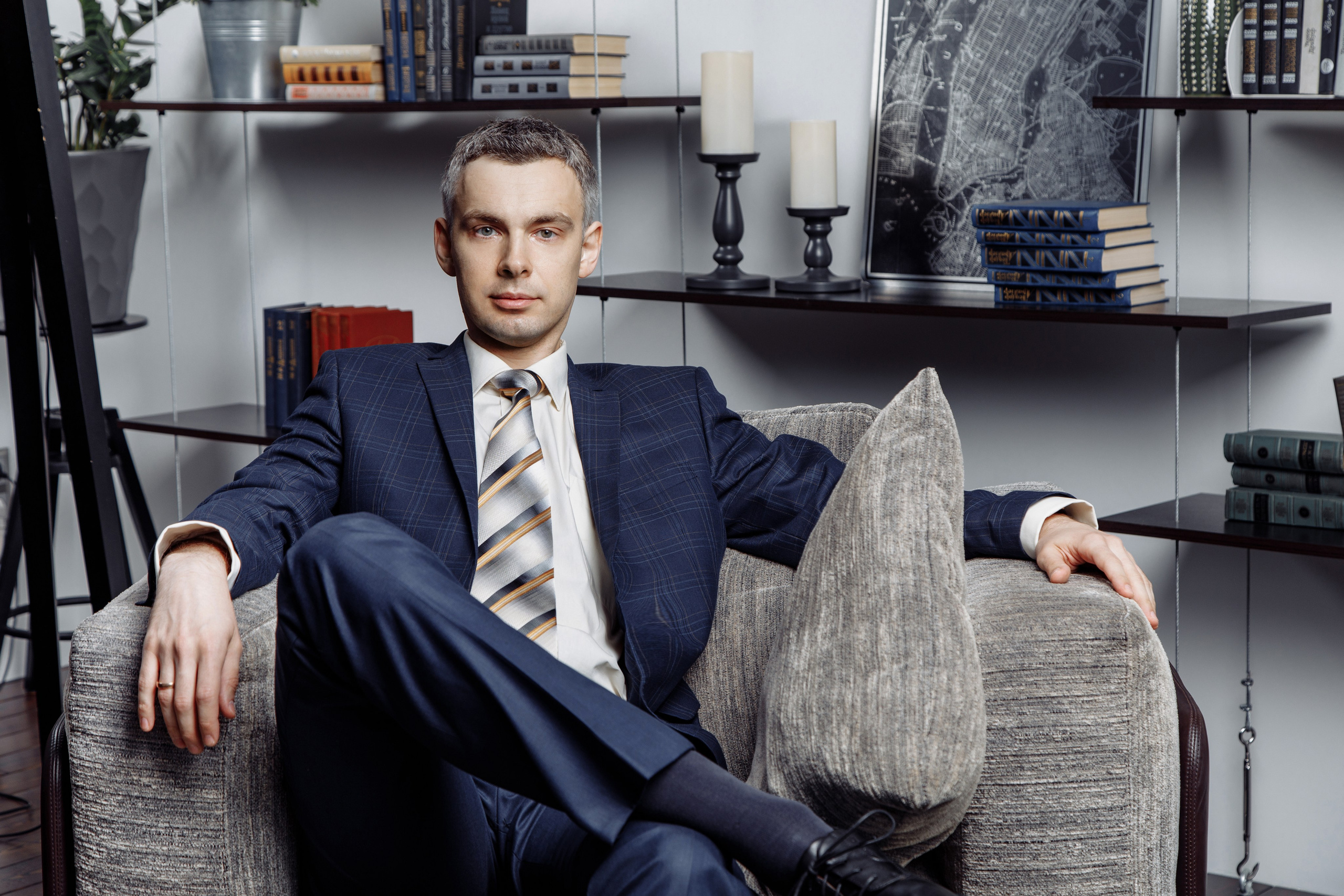 Мужчина в костюме сидит в кресле на фоне открытого офисного пространства.