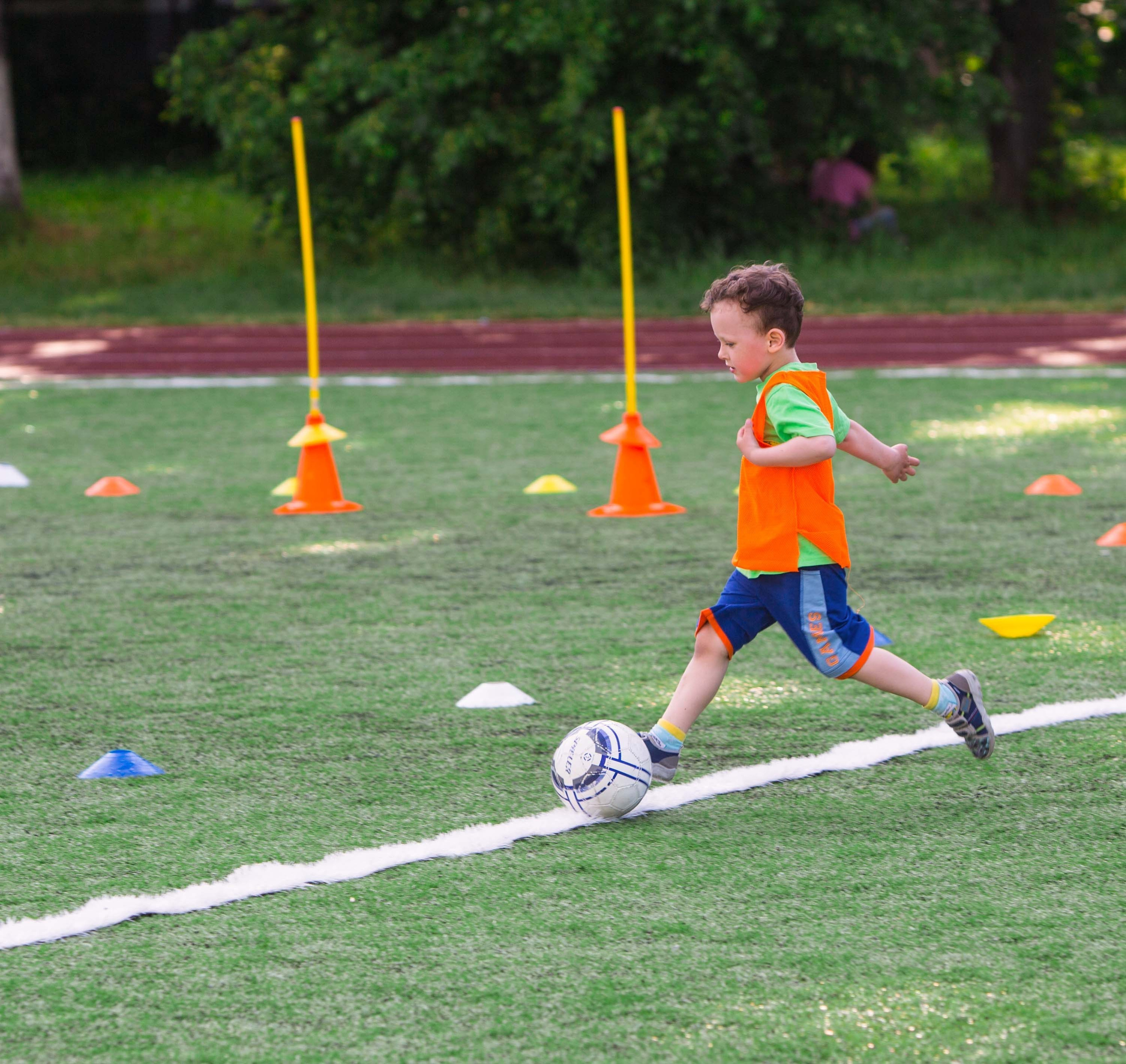 Мальчик ведет мяч через конусы на детской футбольной тренировке