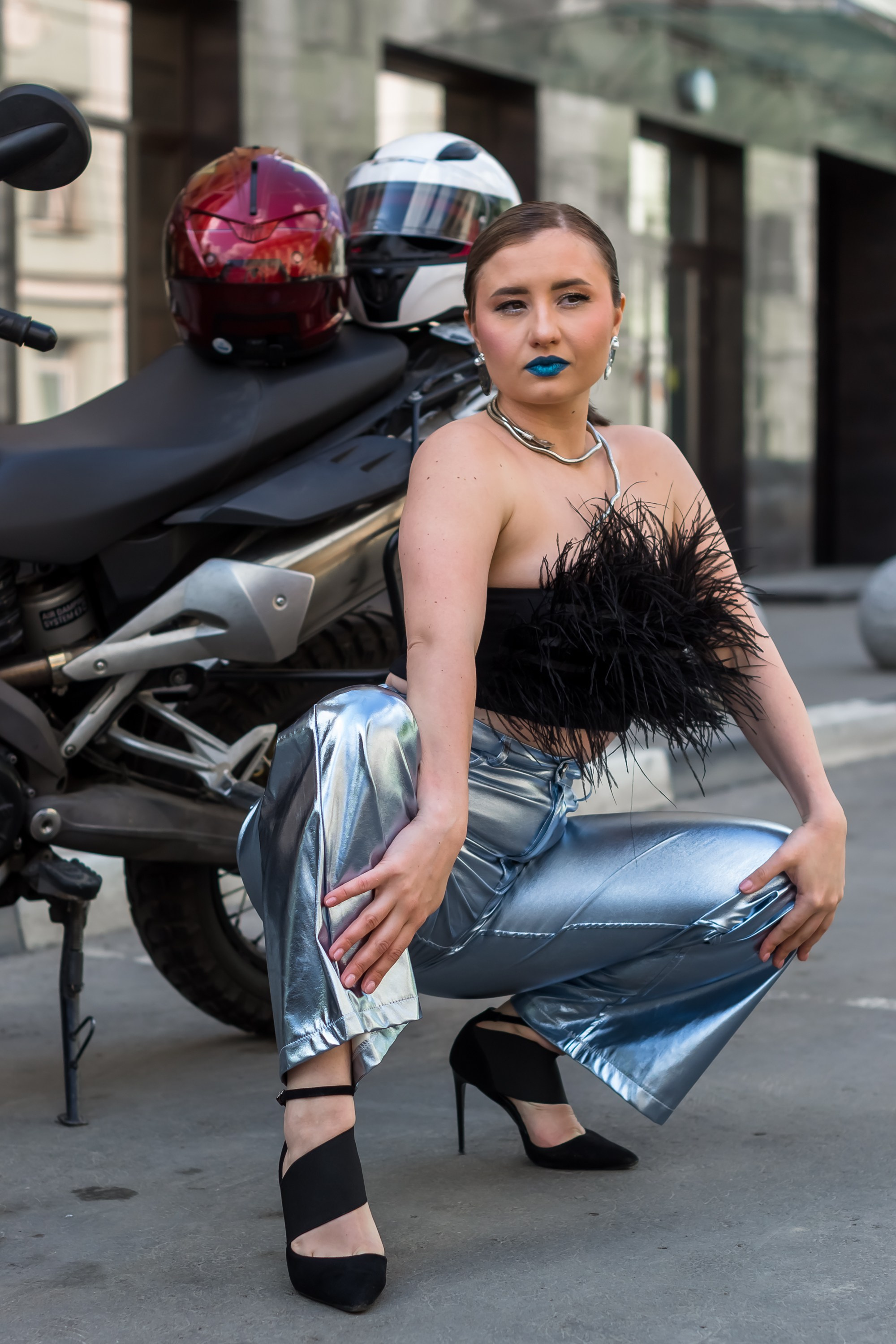 Портрет девушки в брюках сидит на корточках.