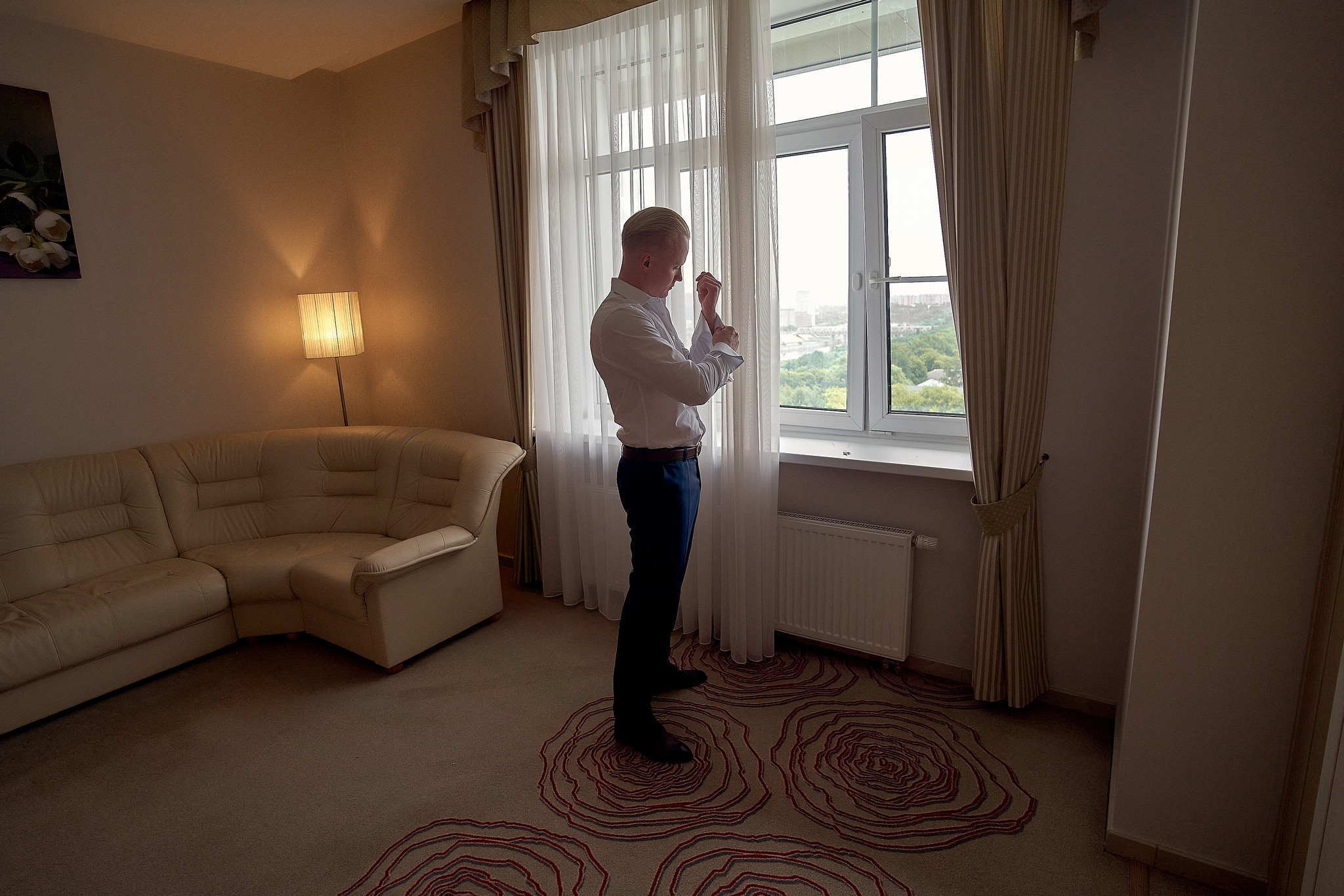 Жених в отеле на фоне окна застегивает рубашку. Свадебный фотограф в Москве Сергей Гаварос. gavaros.ru