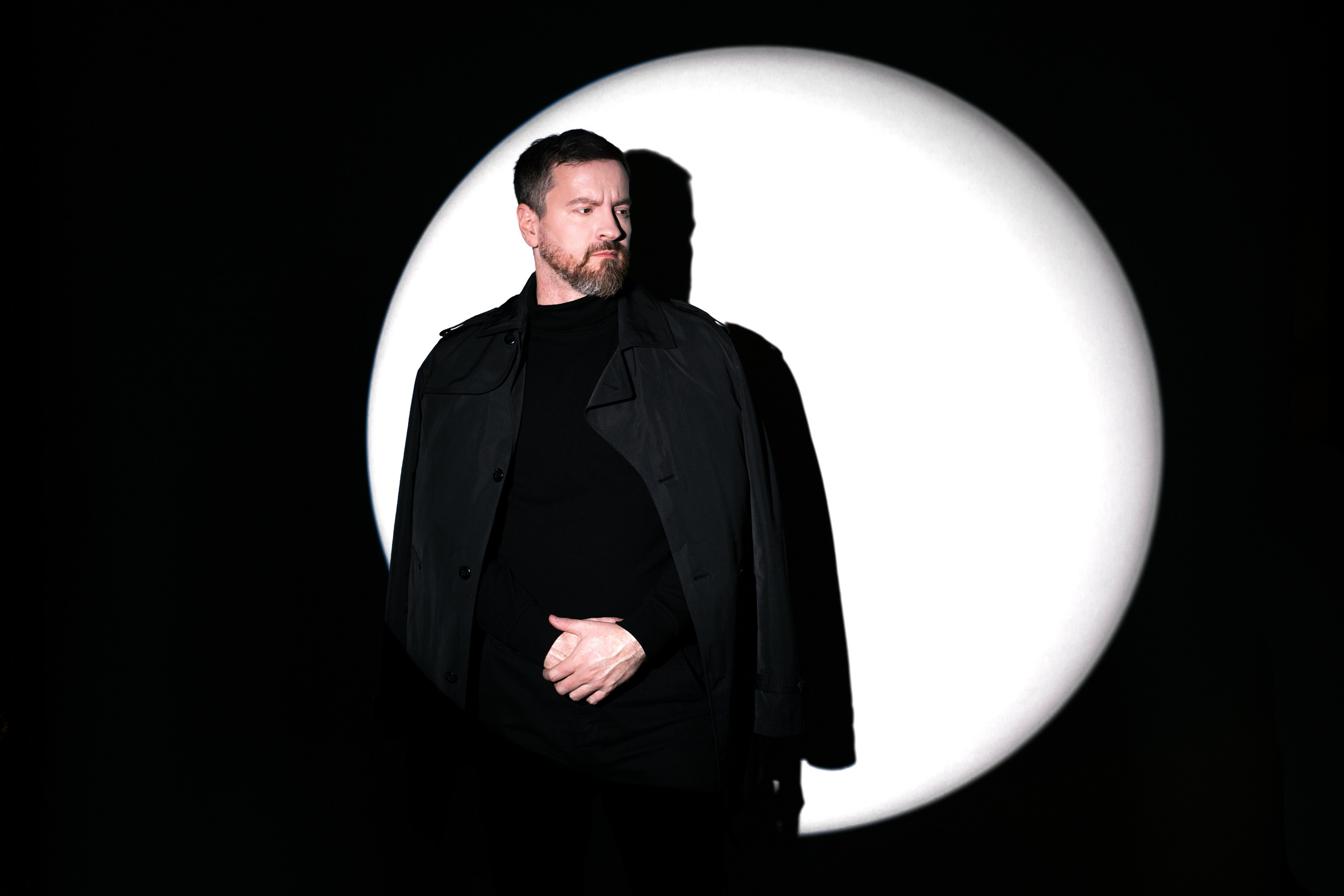 Мужчина в плаще в белом круге света