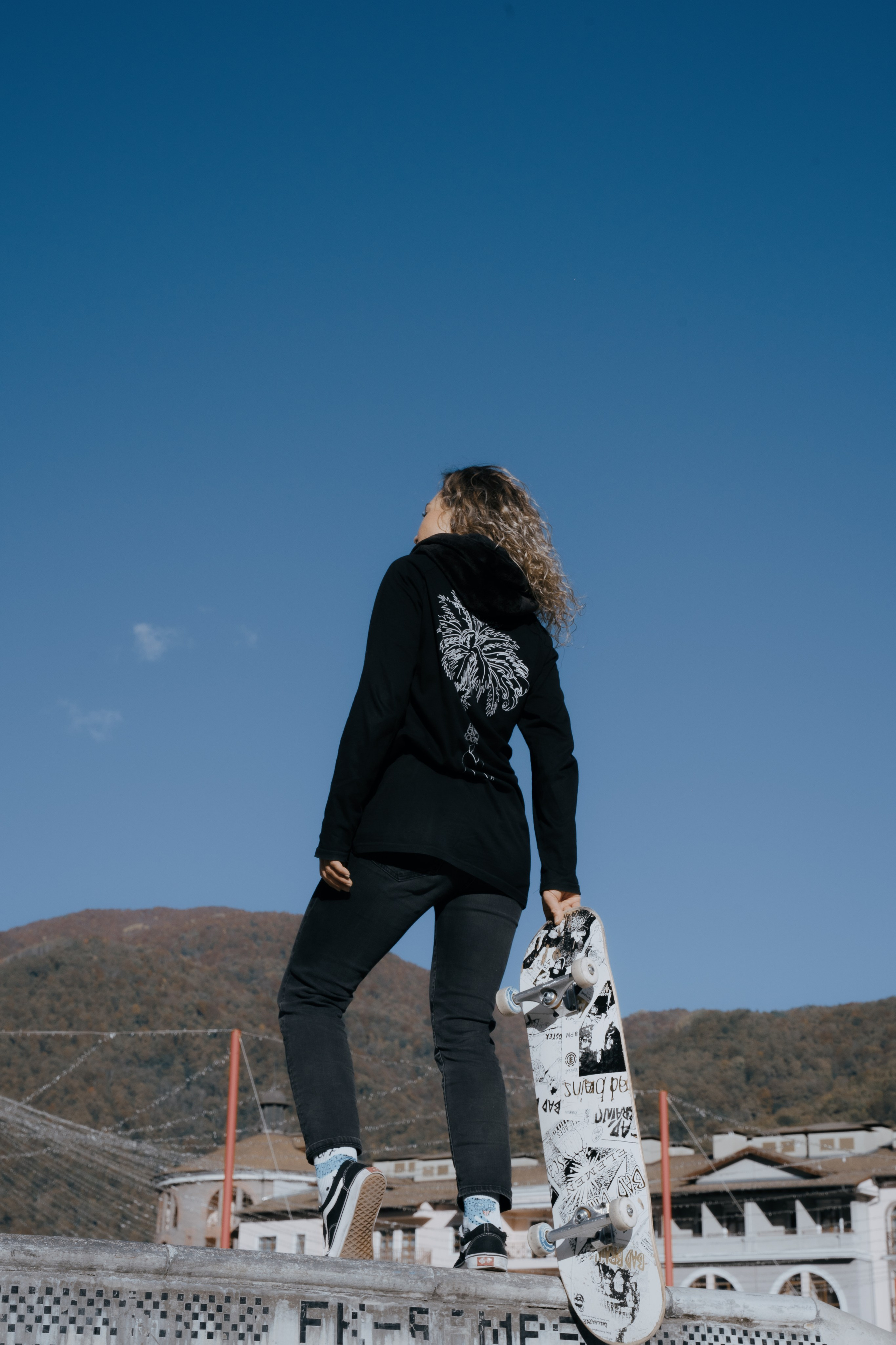 Фотография молодой девушки со скейтом на возвышенности 