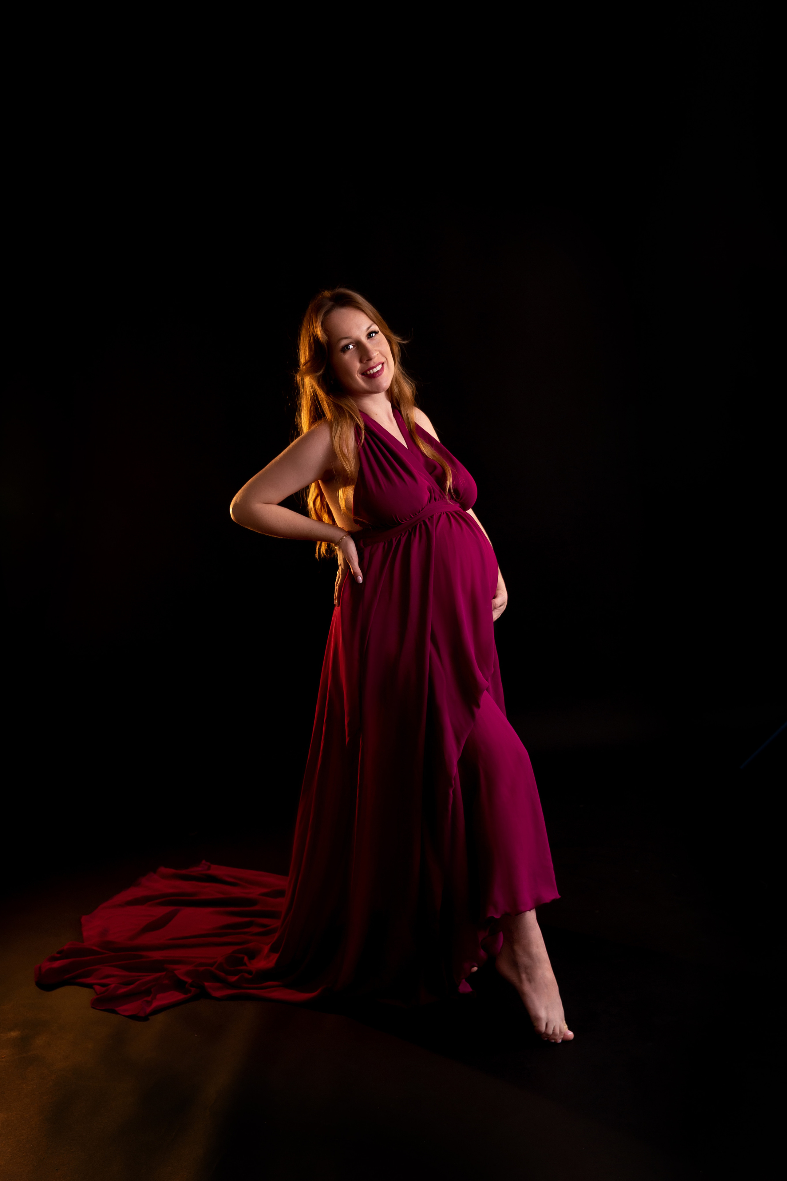 Беременная девушка в платье винного цвета на черном фоне
