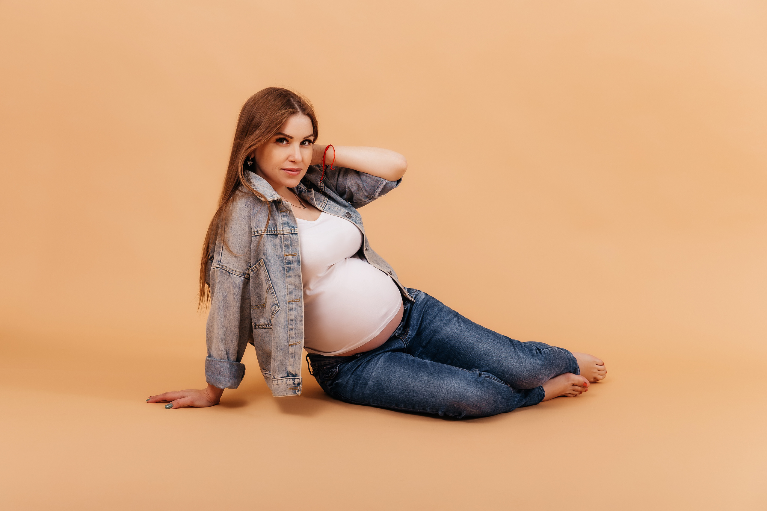 Беременная девушка  в джинсах на светлом фоне