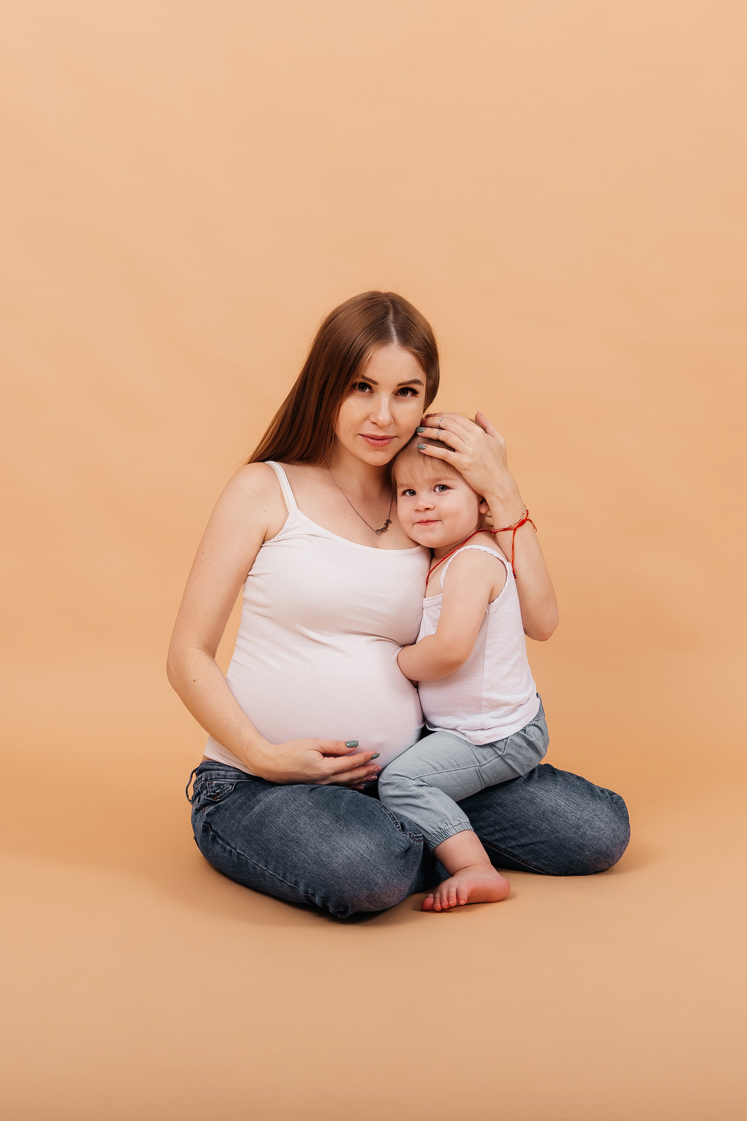 Беременная девушка  в джинсах на светлом фон