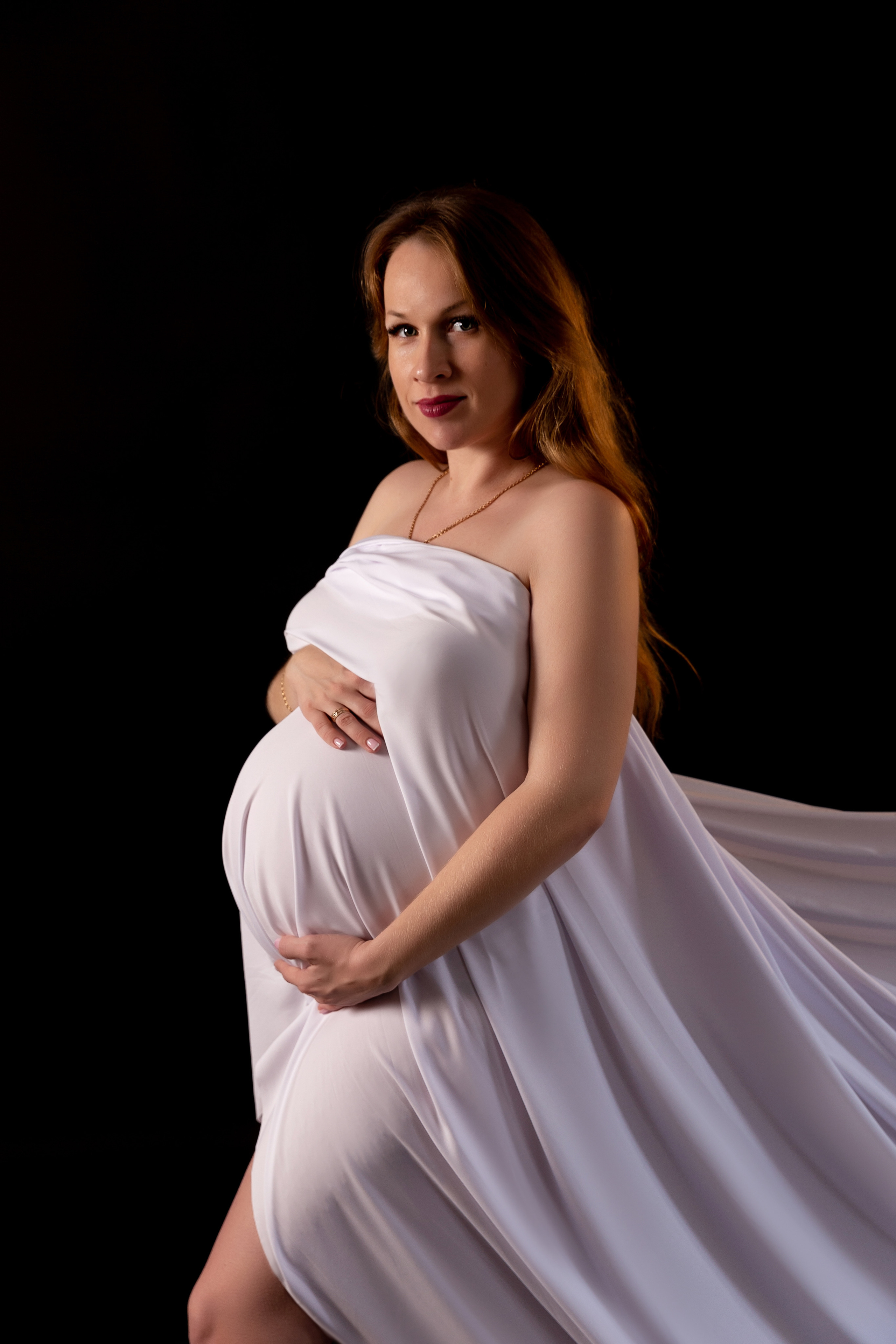 Беременная девушка в белой ткани на черном фоне