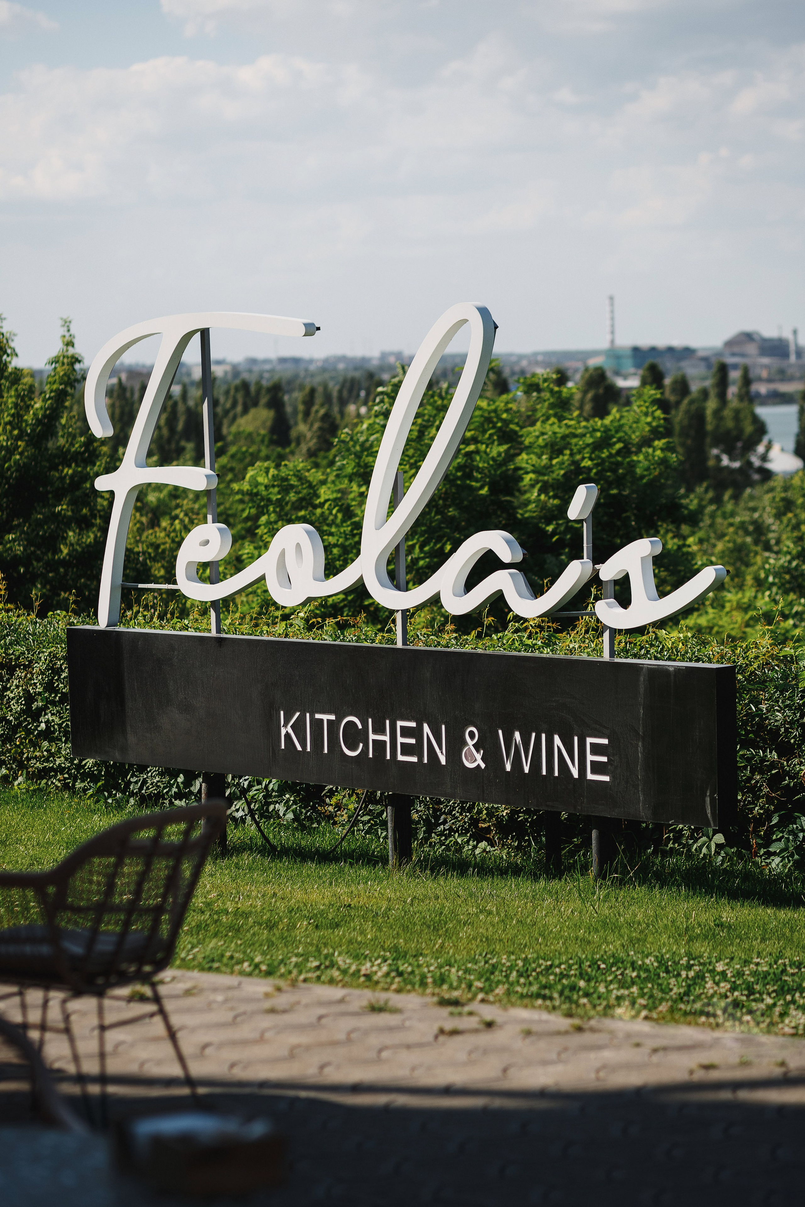 Вывеска ресторана Feola's Kitchen & Wine на фоне зелёной листвы и городского пейзажа.