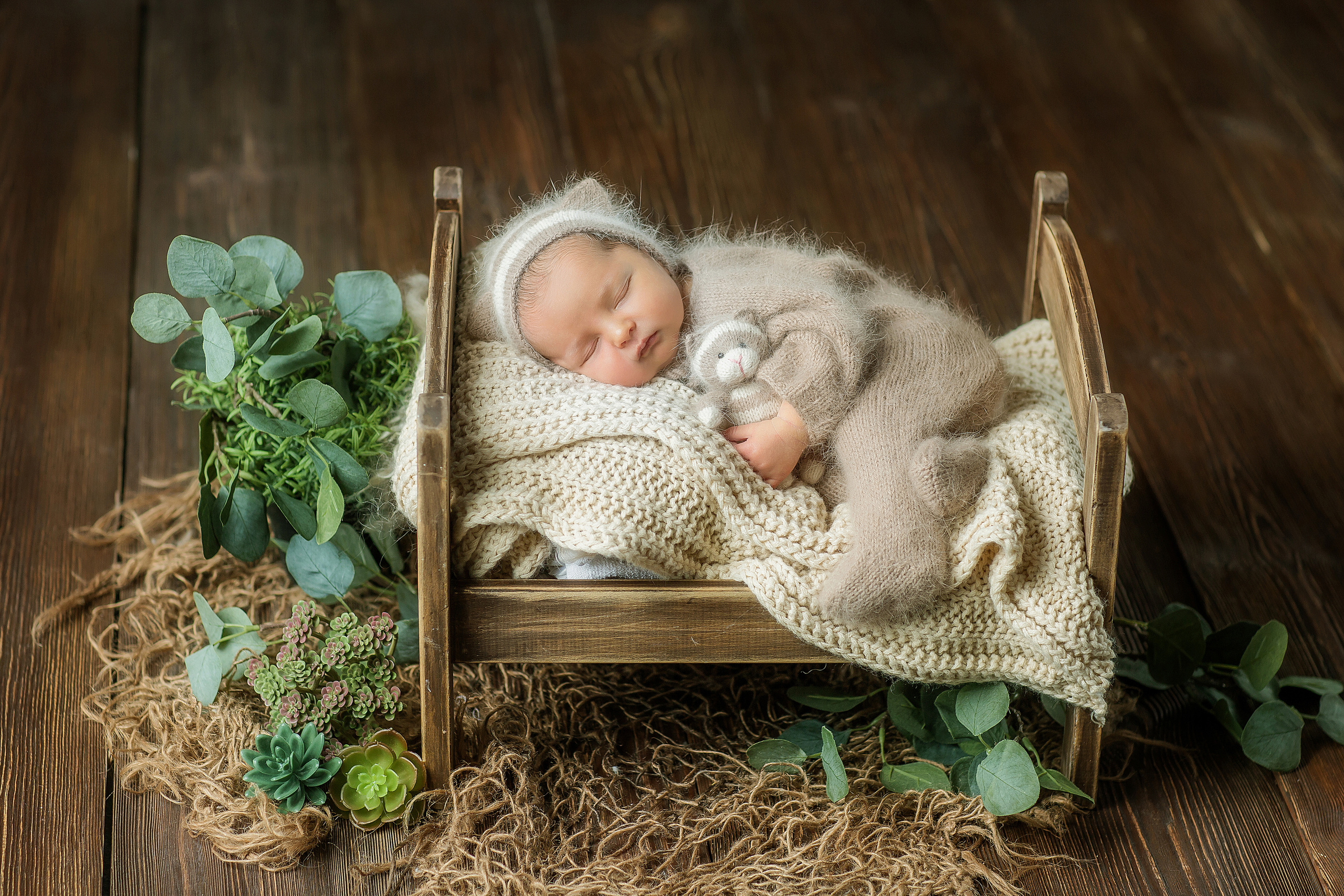 Спящий в крошечной кроватке новорожденный малыш в шапочке котика с игрушкой в руках