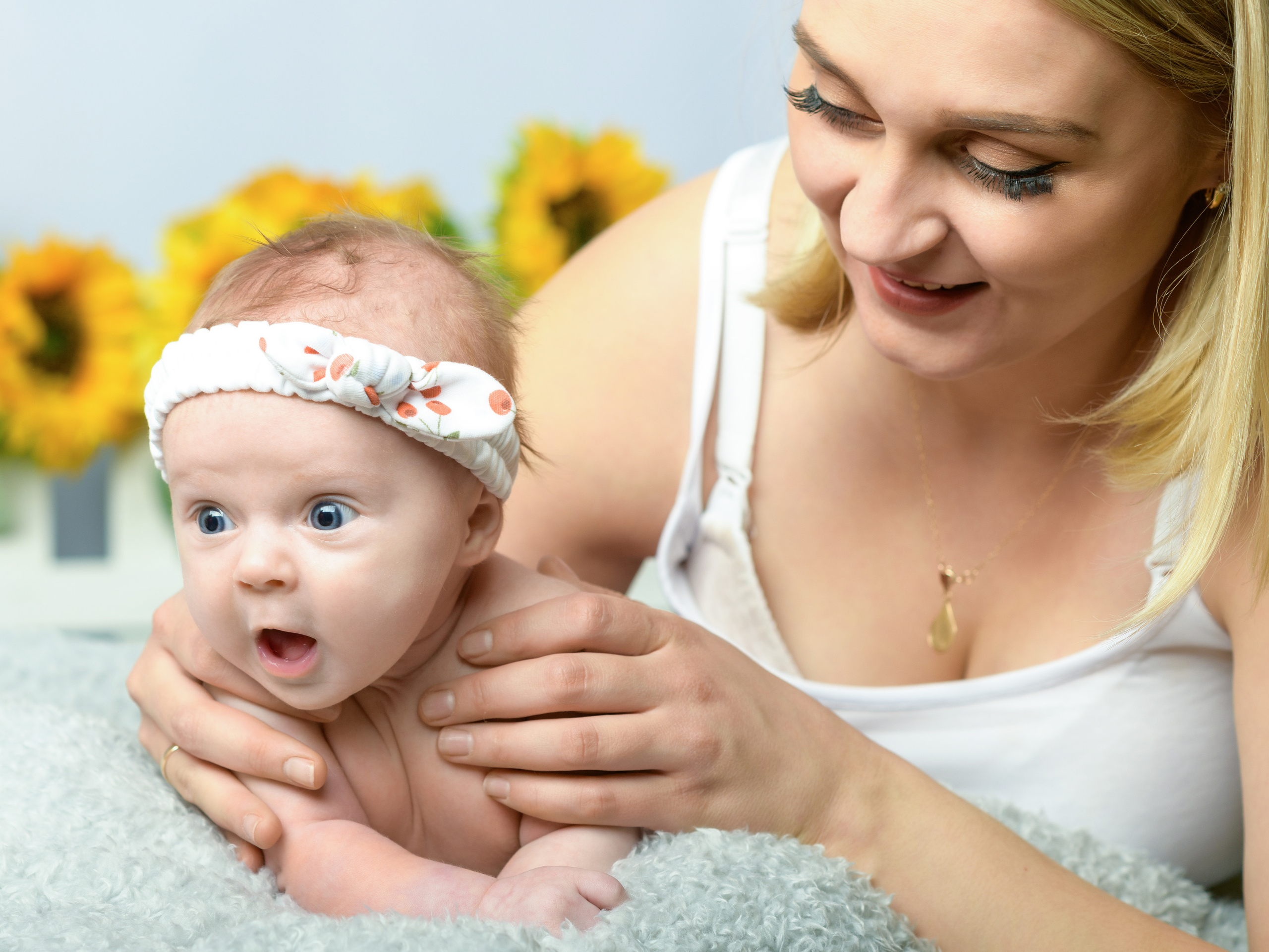 маленькая девочка на руках у заботливой мамы удивленно смотрит на что то