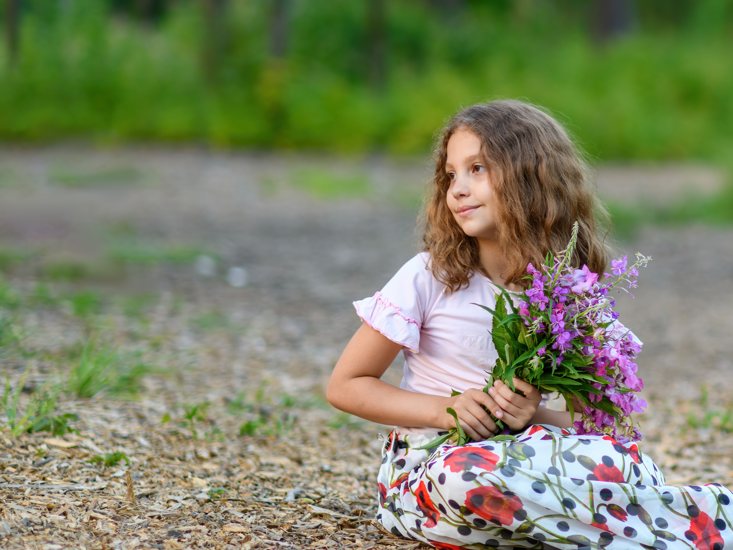 Девочка с букетом сидит на траве и смотрит в сторону отвернувшись от камеры