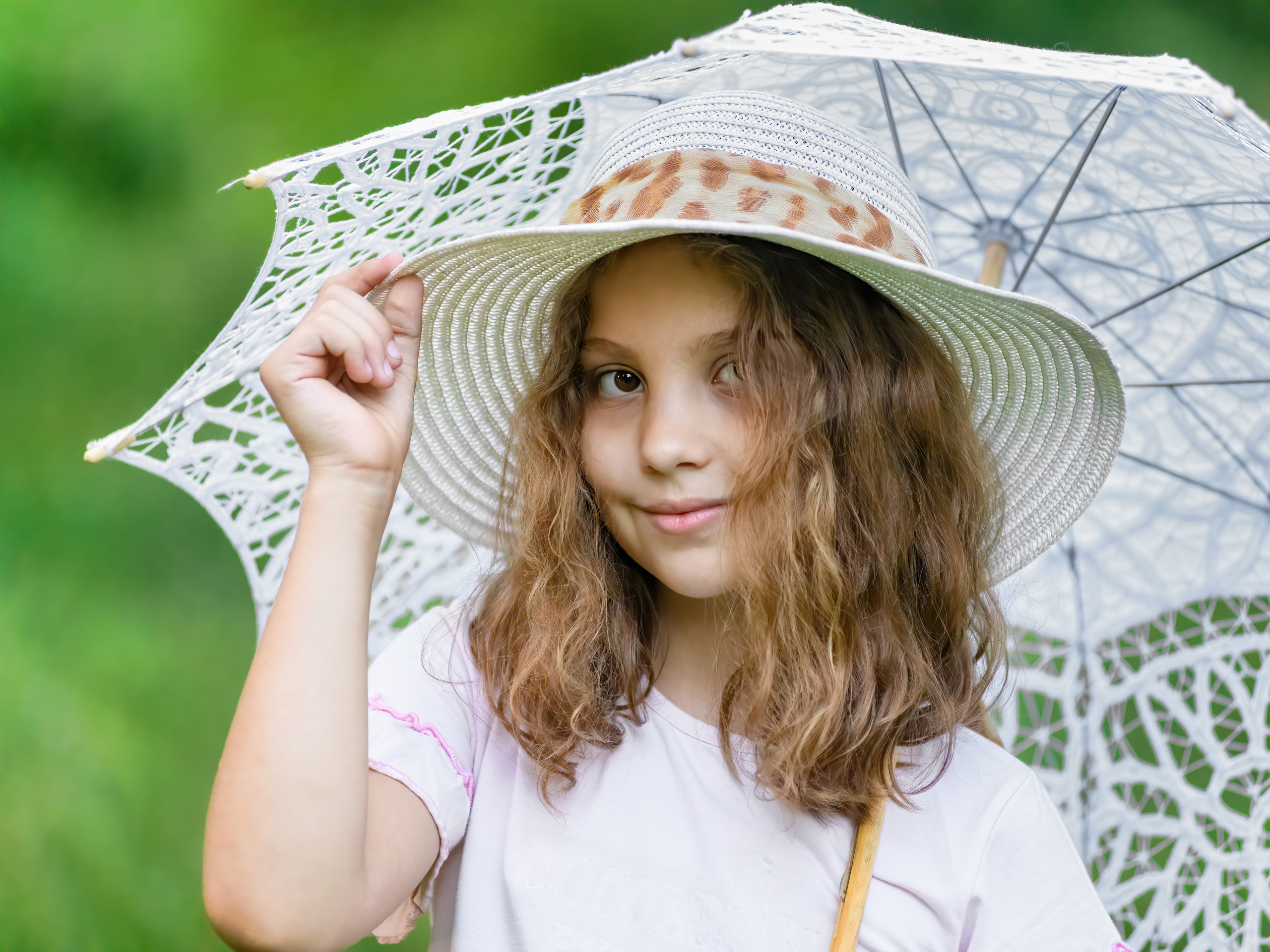 девушка позирует  дежа пальцами за поля шляпку и с зонтом на плече в парке 