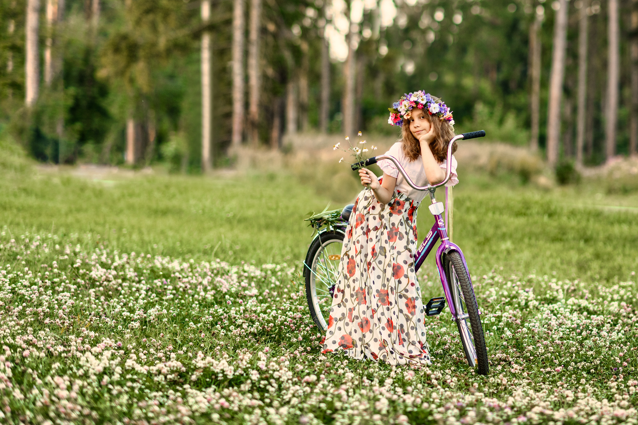 Девушка стоит с велосипедом посередине поля усыпанного цветущей кашкой