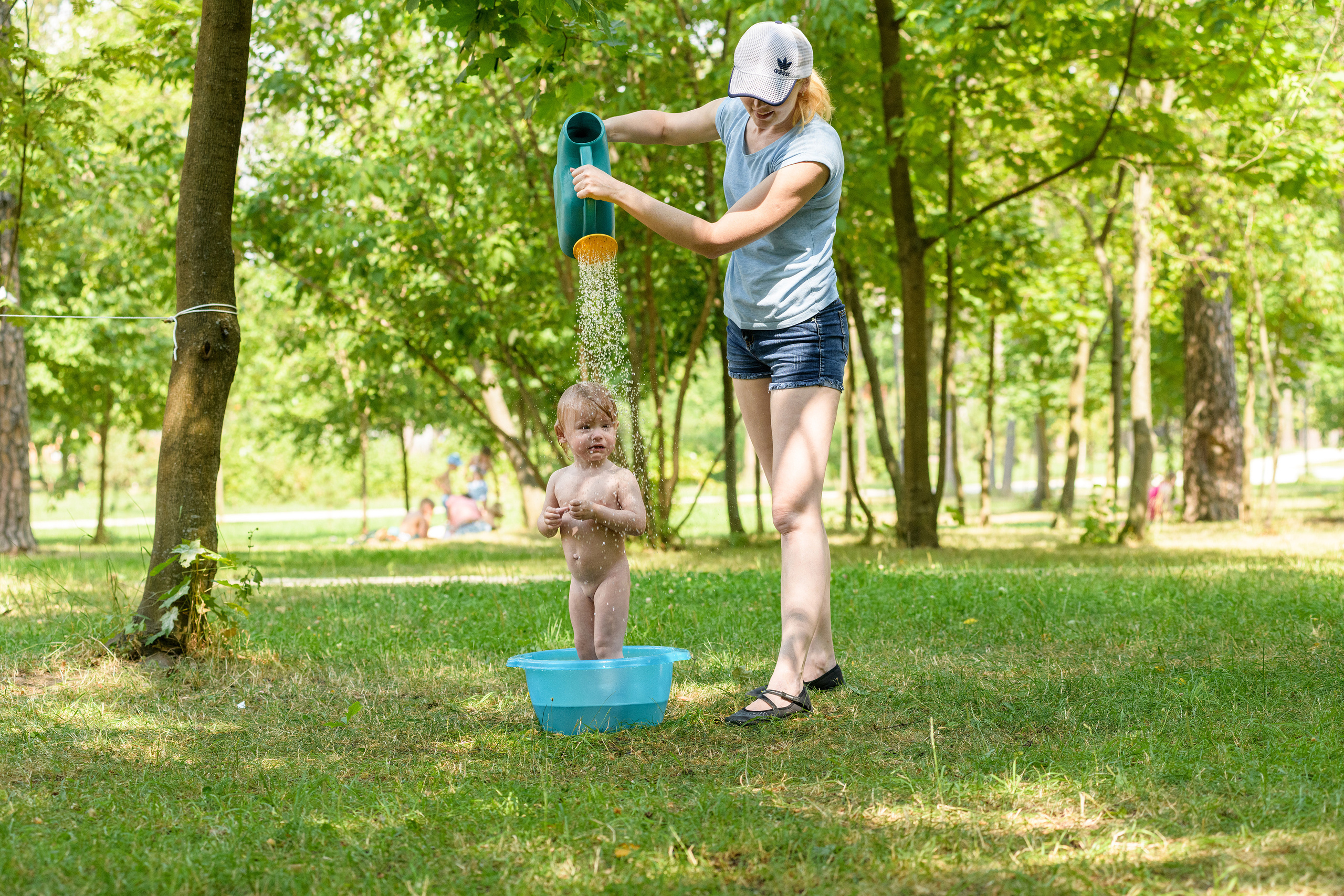 парк летом мама поставила малышку в тазик и поливает ее из лейки водой